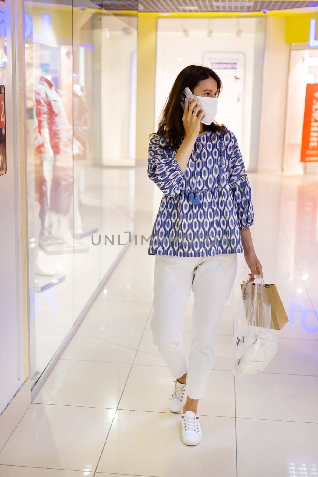 A young girl carrying shopping bags walks through a mall wearing a medical mask during the coronavirus pandemic