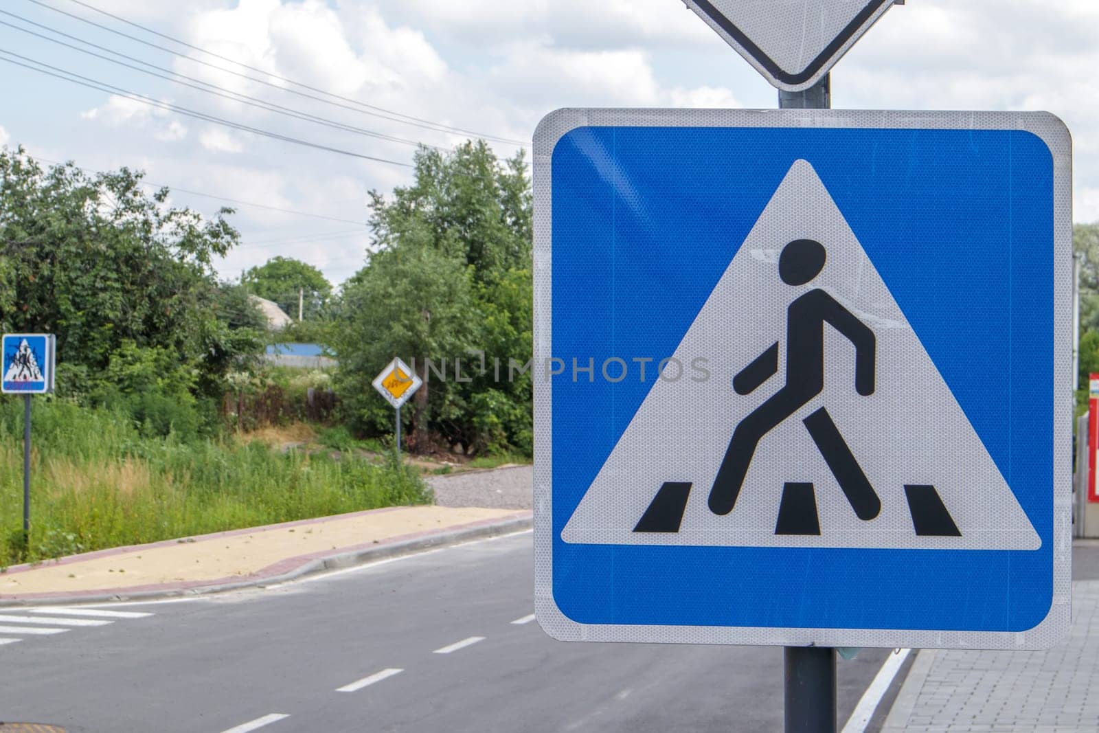 Pedestrian overground crossing, old square white with blue reflective road sign, outdoors close-up. Zebra and human sign on the background of the city. Pedestrian crossing sign