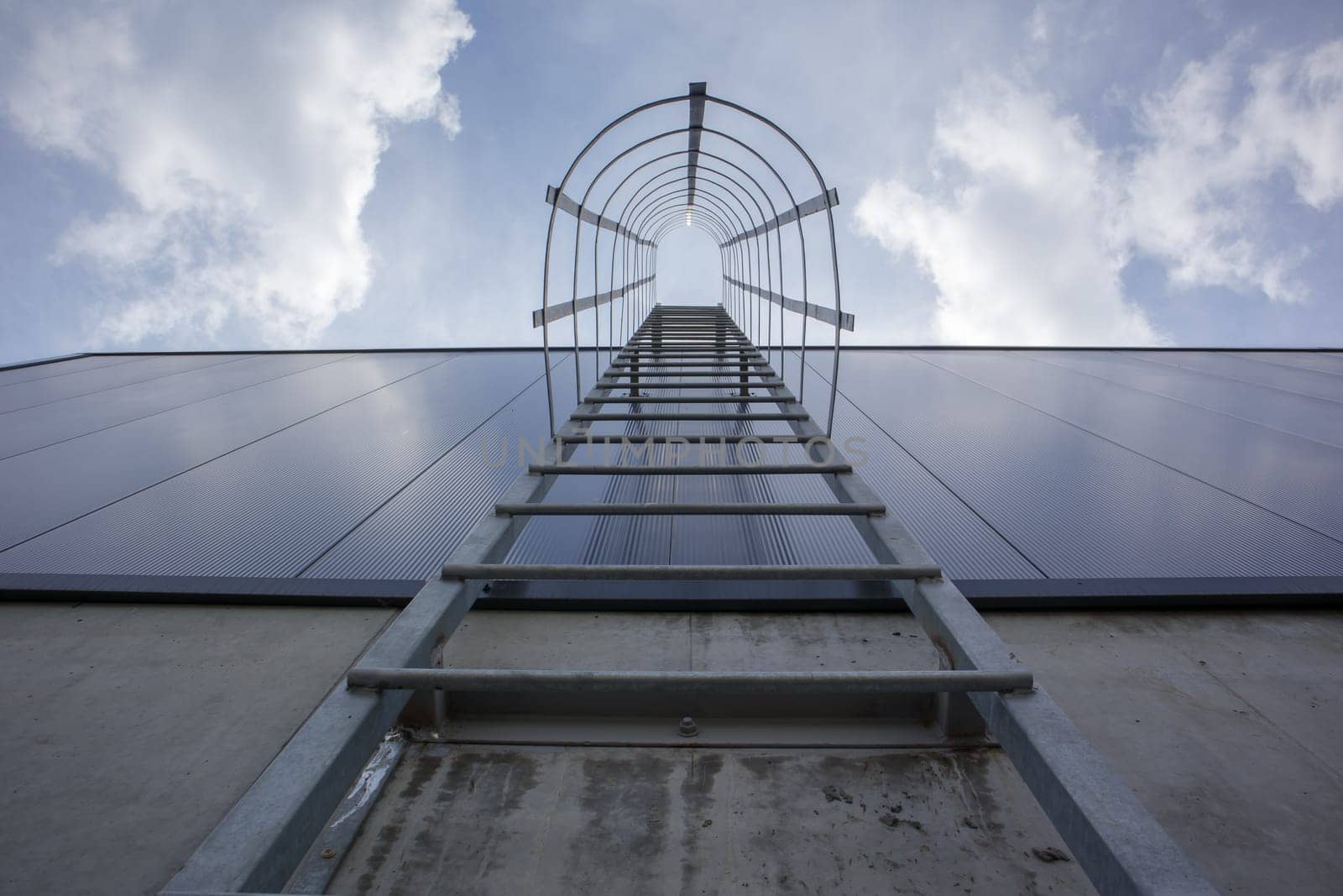 Fire escape on the industrial building above, bottom view. Stainless steel handrails, roof ladder. Detail view of stairs with safety cage. Building construction concept