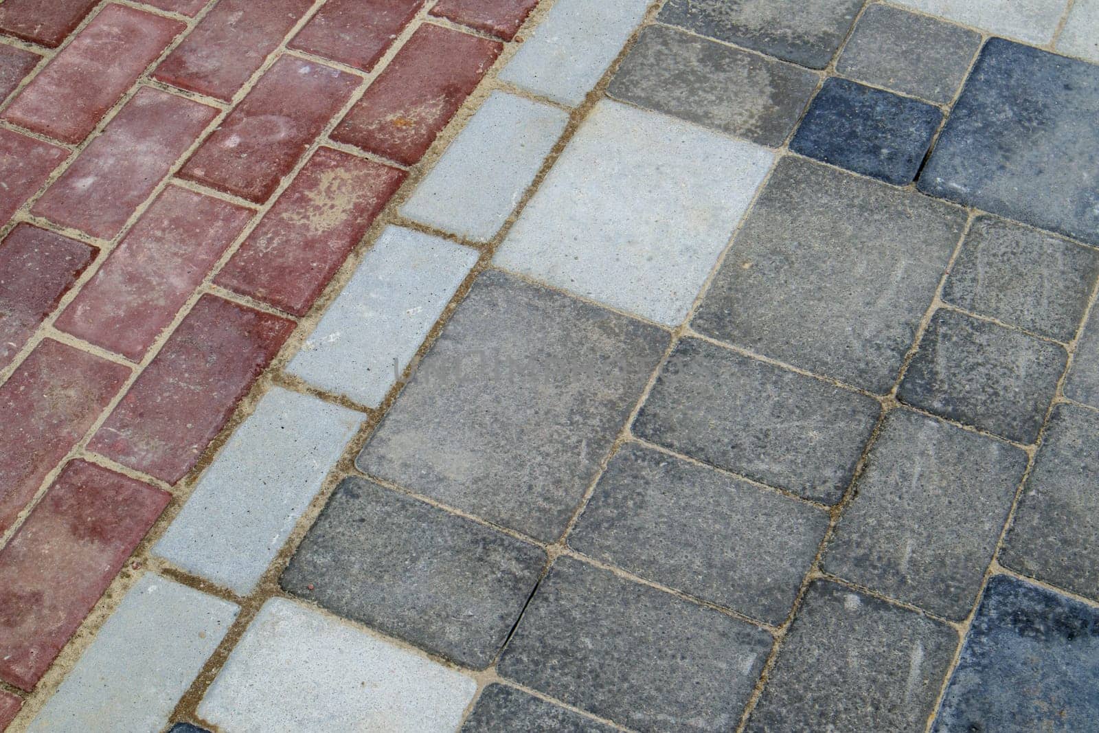 Concrete or paved newly laid gray and red paving slabs or stones for floors or walkways. Concrete paving slabs in the backyard or road paving. Garden brick path in the courtyard on a sandy foundation