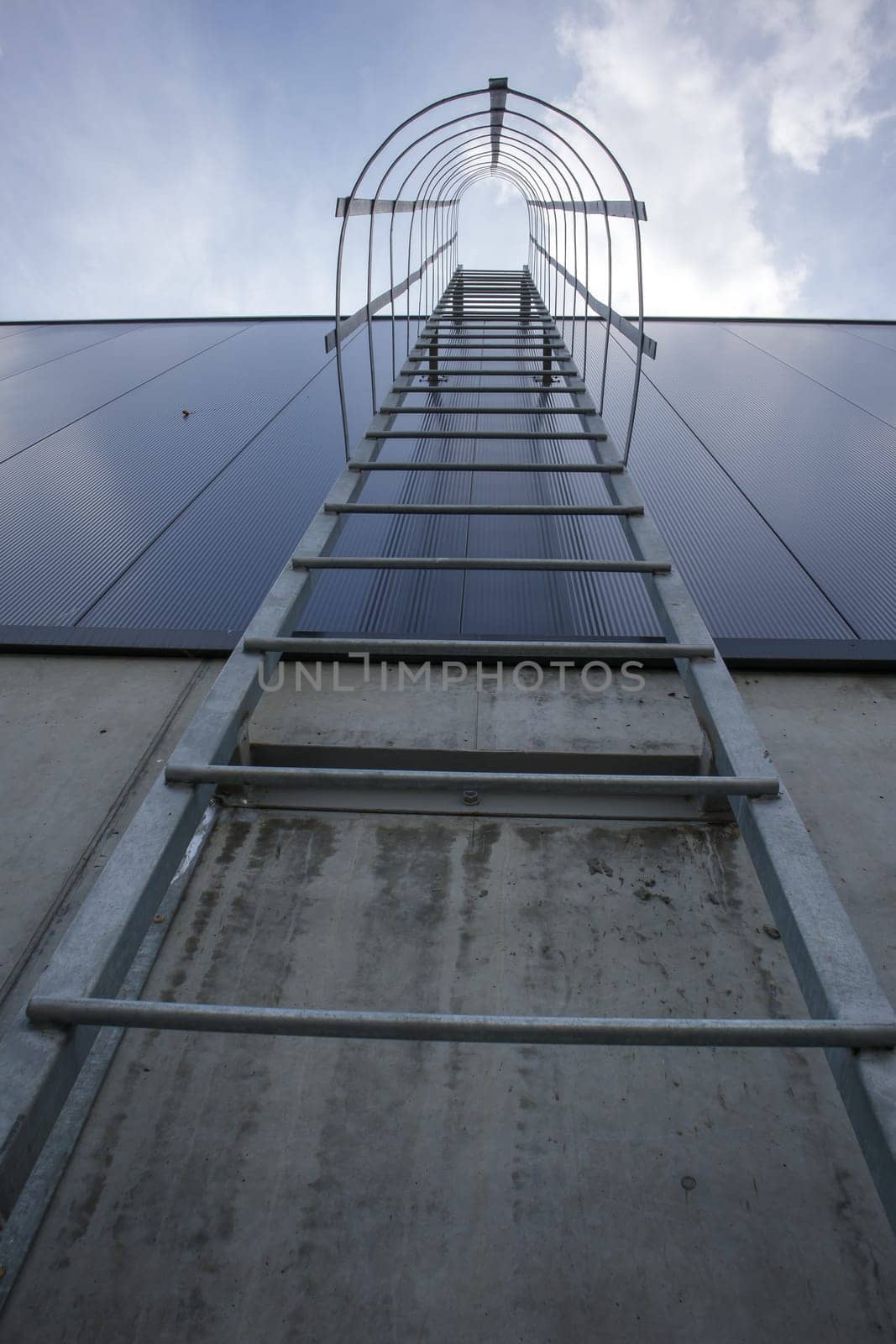 Fire escape on the industrial building above, bottom view. Stainless steel handrails, roof ladder. Detail view of stairs with safety cage. Building construction concept