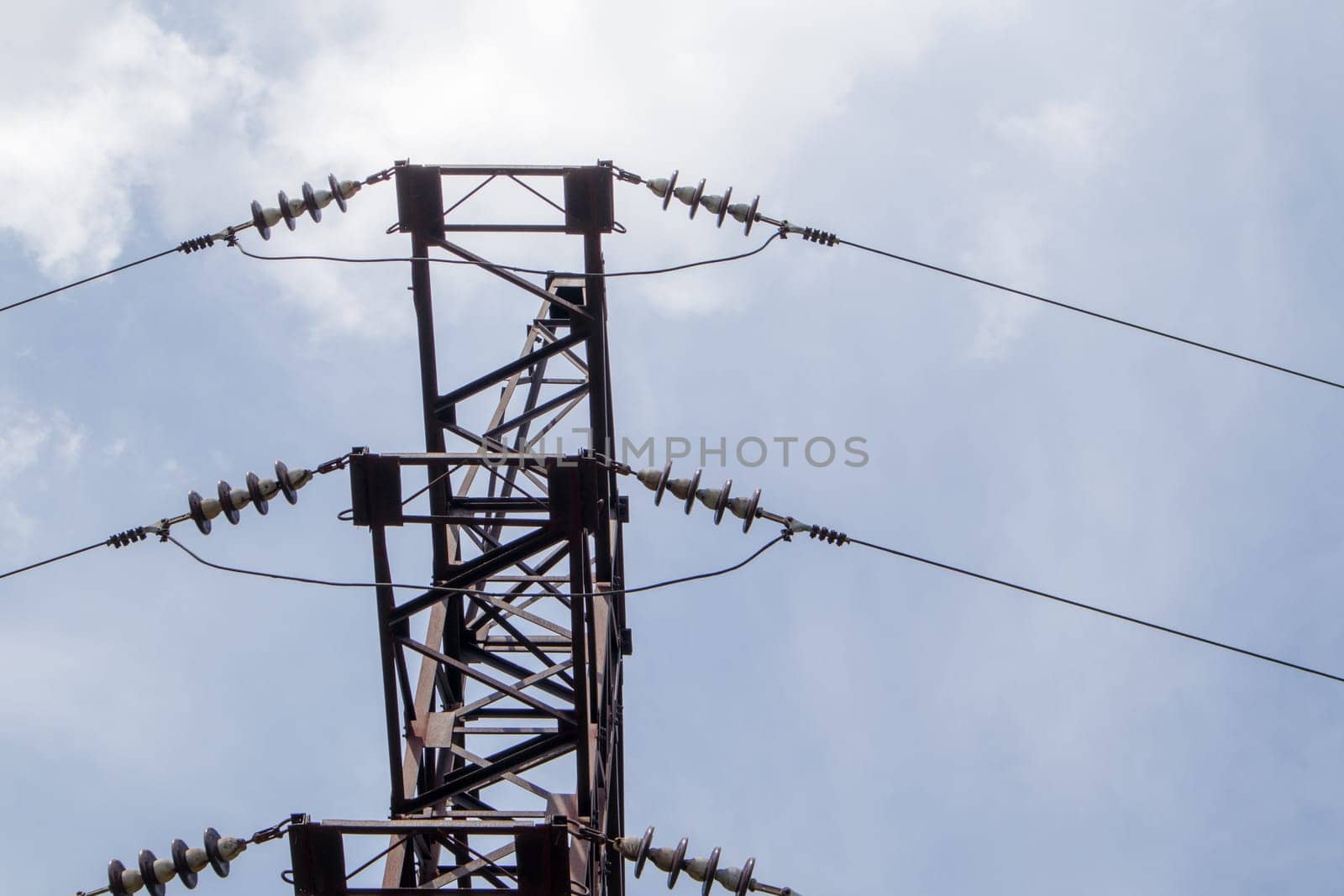 High voltage electrical tower. Power lines and power pylons on a sunny day with circular clouds in the blue sky. High voltage power transmission line supports. They have a complex steel structure