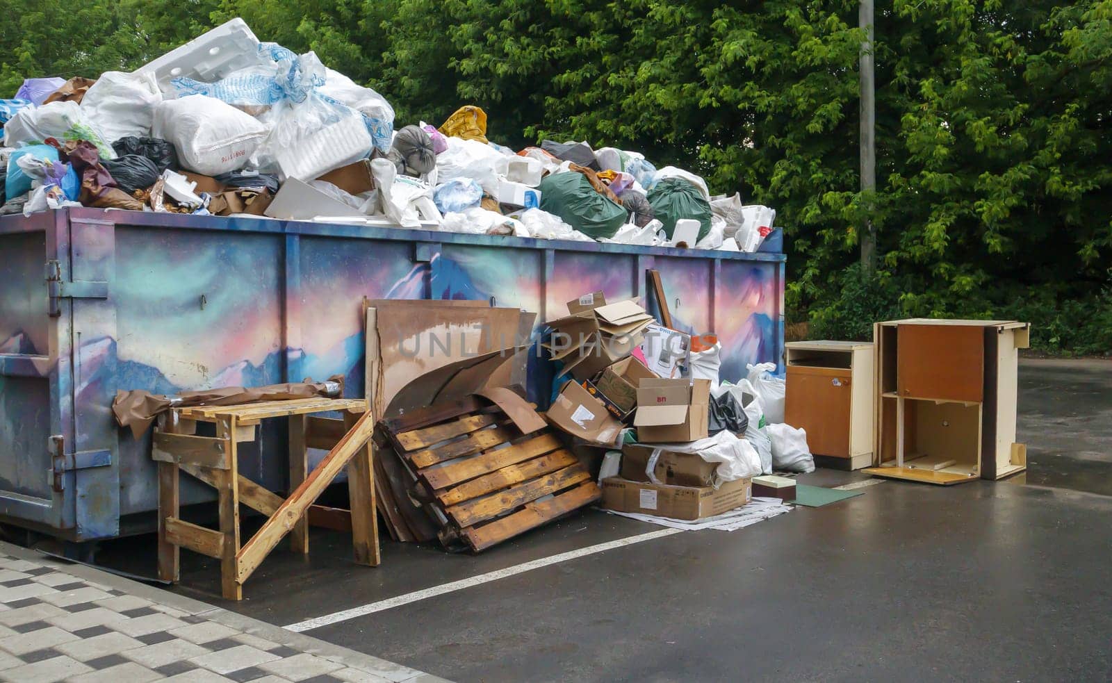 Metal durable blue industrial trash bin for outdoor trash at construction site. Large waste basket for household or industrial waste. A pile of waste. Ukraine, Kiev - August 09, 2021