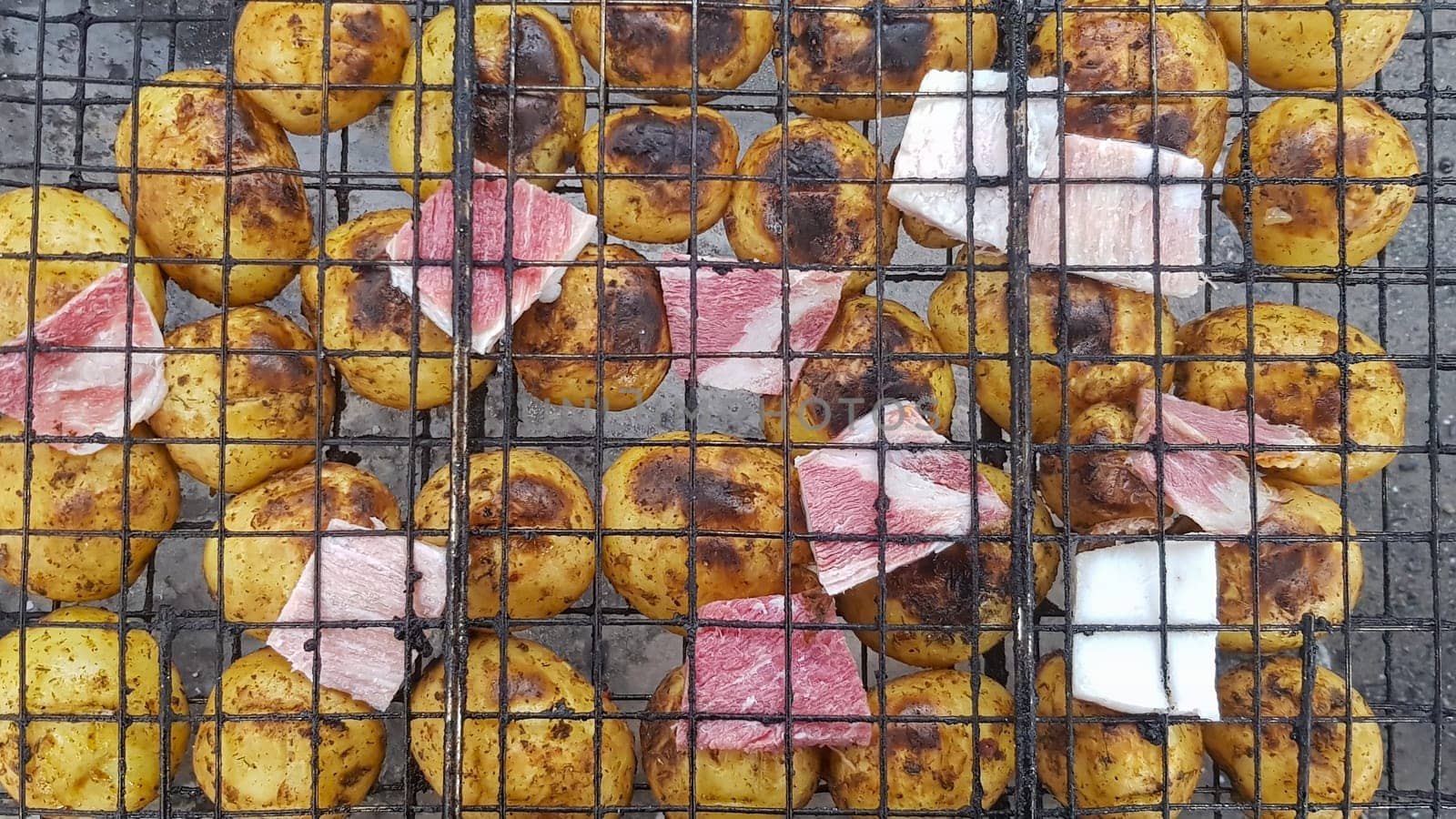 Grilled potatoes with bacon, whole baked on the barbecue grill. Selective focus. Whole small potatoes with bacon bits and grilled. Baked potatoes with grilled bacon