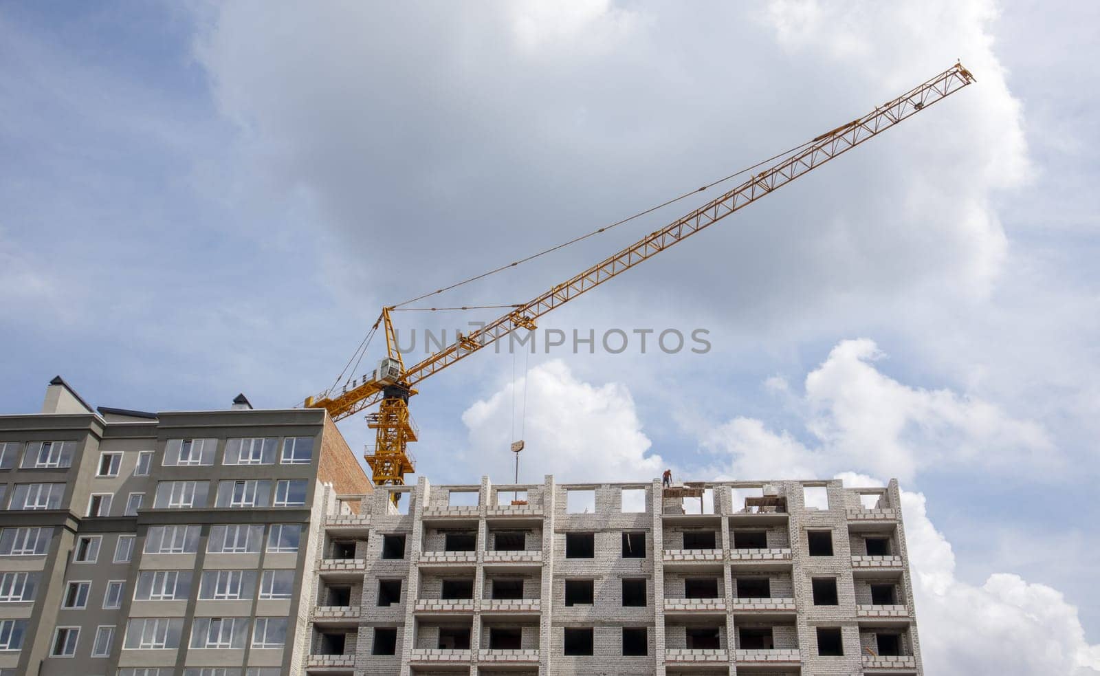 Construction crane on an unfinished residential building against the sun and blue sky. Housing construction, apartment building in the city. Construction site of residential buildings