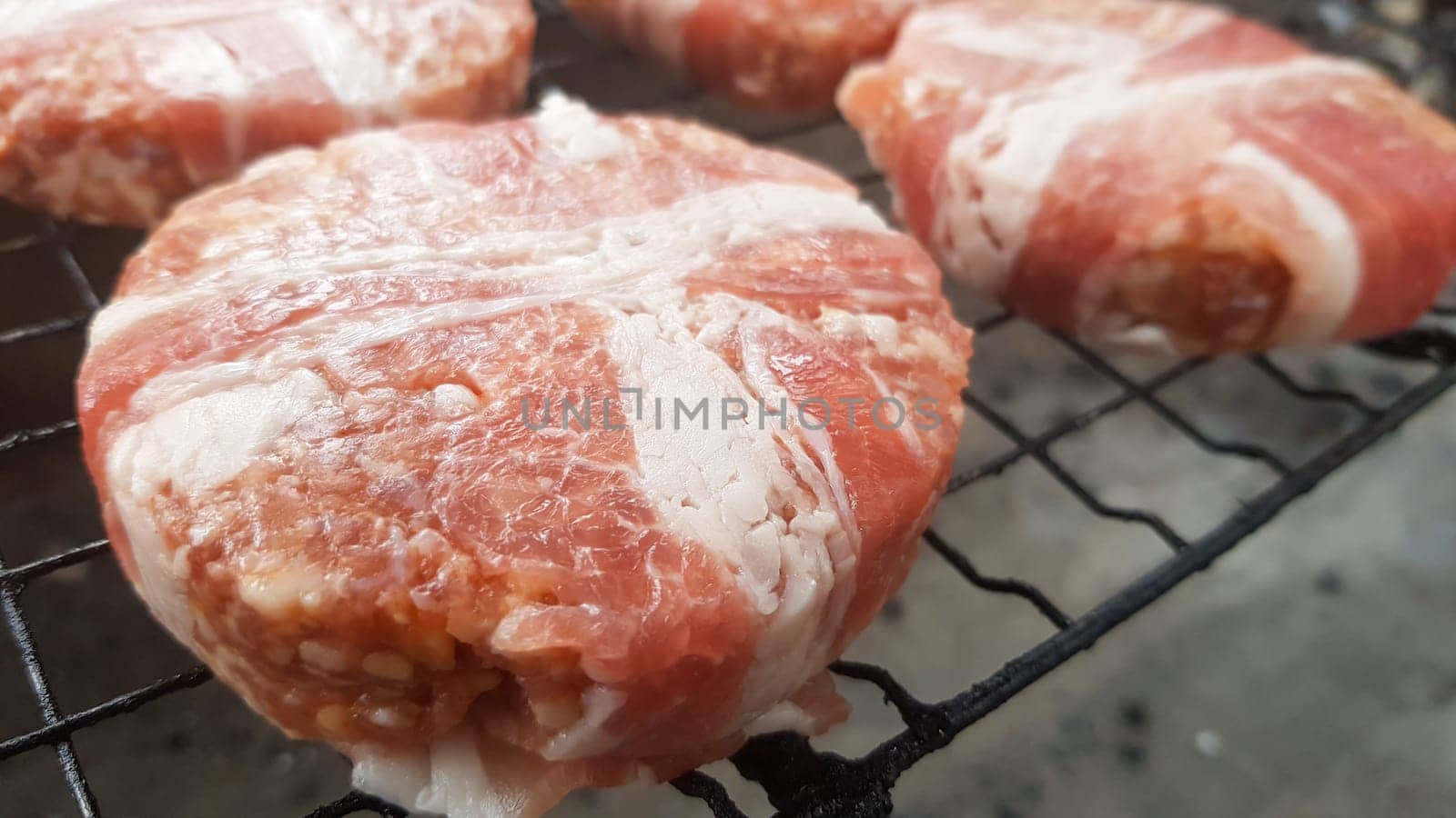 Raw meat cutlets wrapped in bacon are cooked on the grill rack. The chef prepares the grilled burger patties. Ingredients for making a hamburger. Meat lovers concept. Fast food