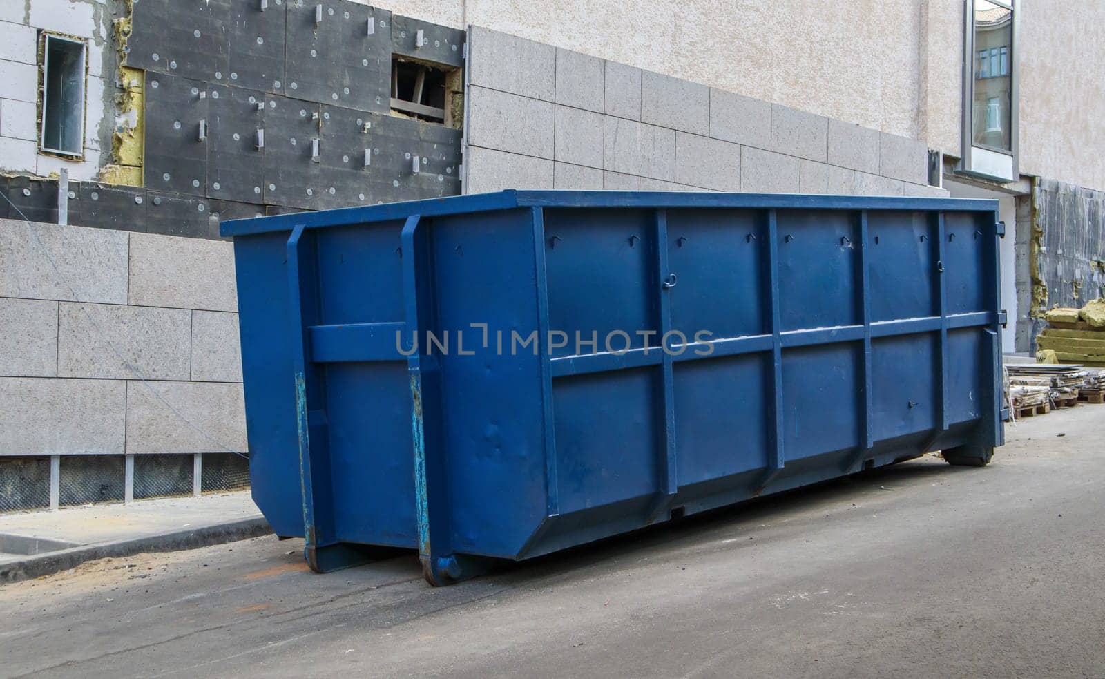 Metal durable blue industrial trash bin for outdoor trash at construction site. Large waste basket for household or industrial waste. A pile of waste
