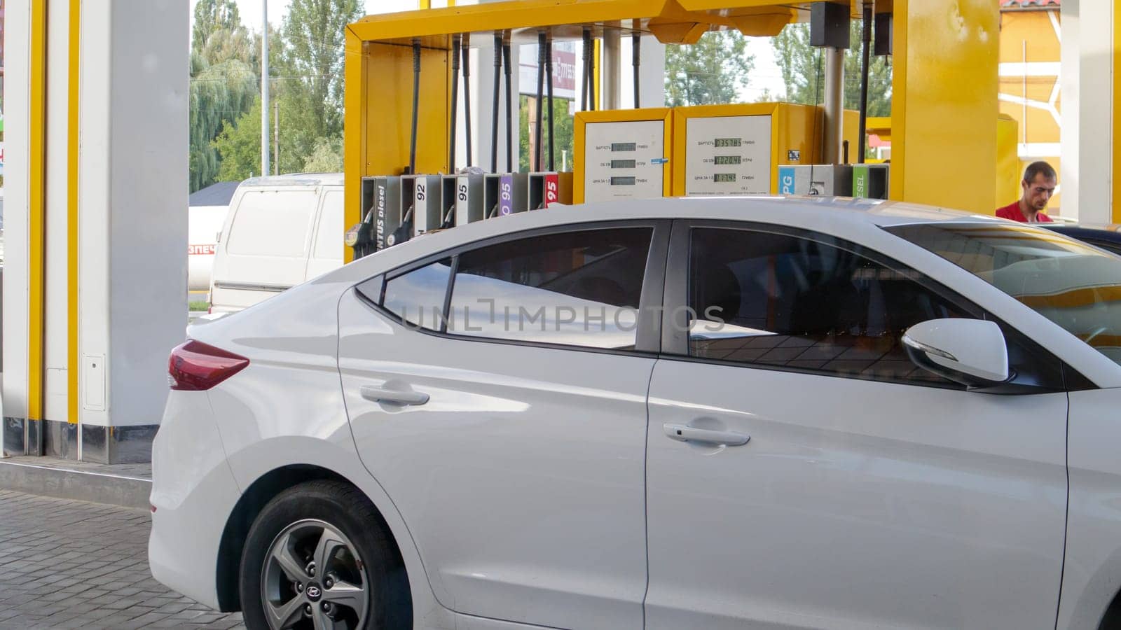 The white car is refueling. Refueling a car that is parked at a gas station. Refuel cars with a gasoline pump. Oil and gas energy. Ukraine, Kiev -15 August, 2021