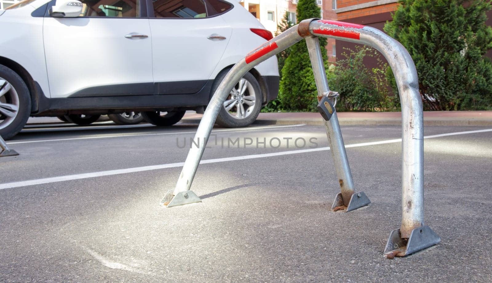 Manual gray galvanized metal parking barrier with lock. Parking lock device. Parking barrier installed. A foldable barrier prevents the vehicle from stopping at this point. Reserved seat