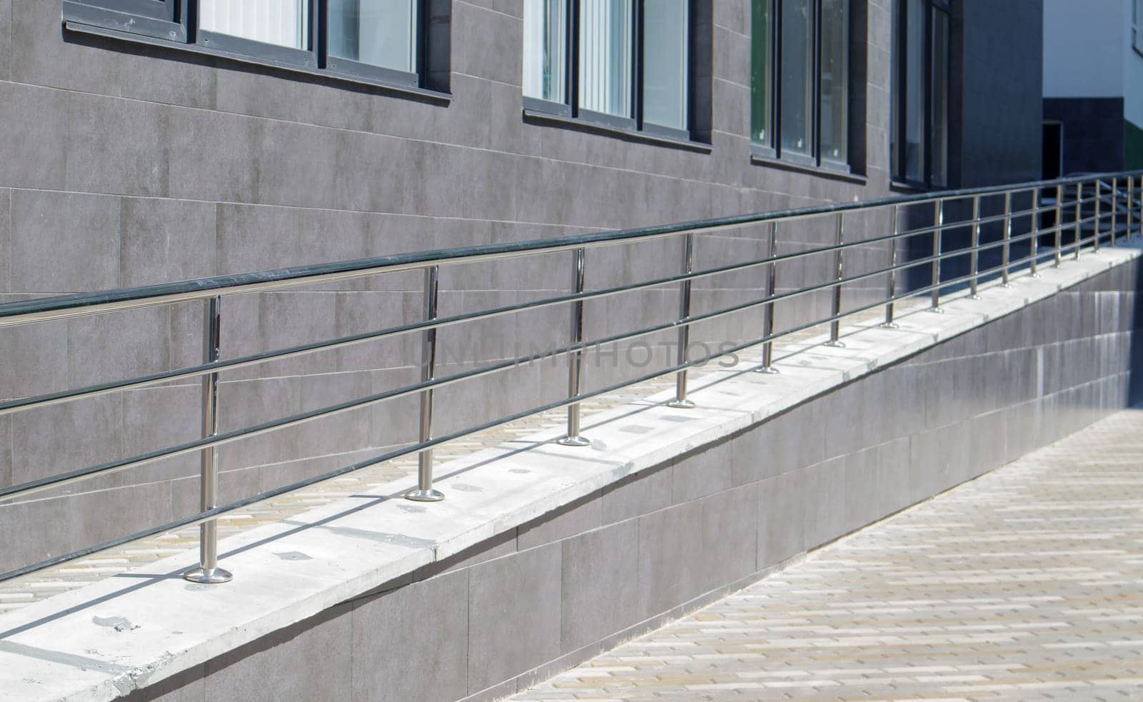 A ramp with stainless steel handrails for wheelchairs, bicycles and strollers with children in front of the building. Handrail for lifting a wheelchair. Shiny stainless steel handrail