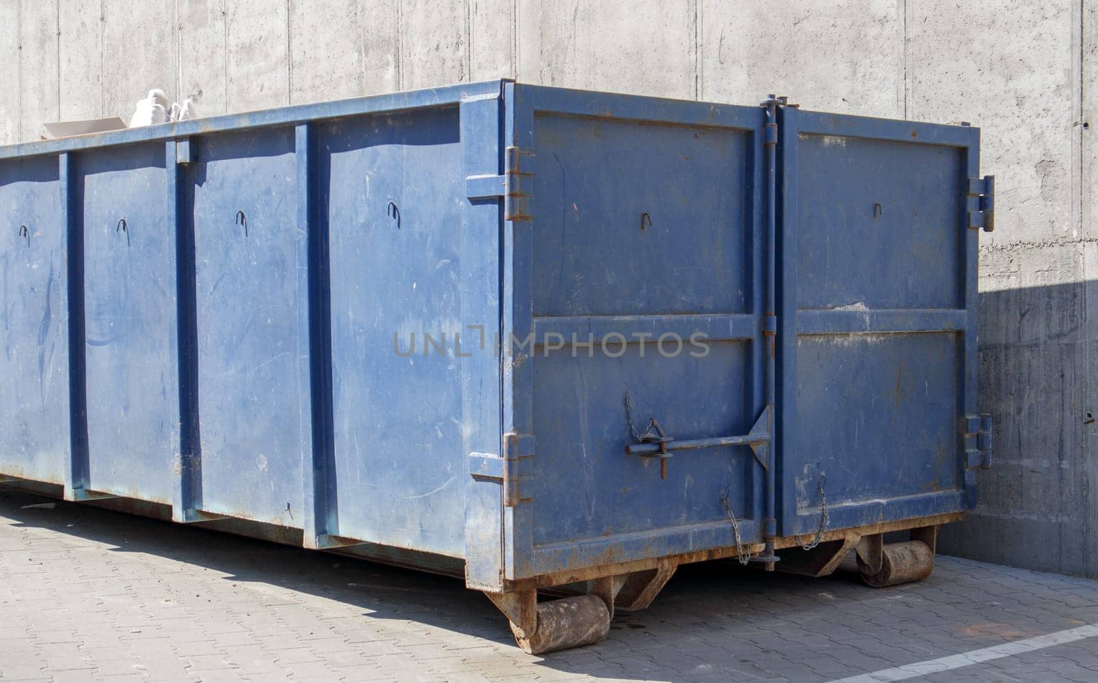 Metal durable blue industrial trash bin for outdoor trash at construction site. Large waste basket for household or industrial waste. A pile of waste