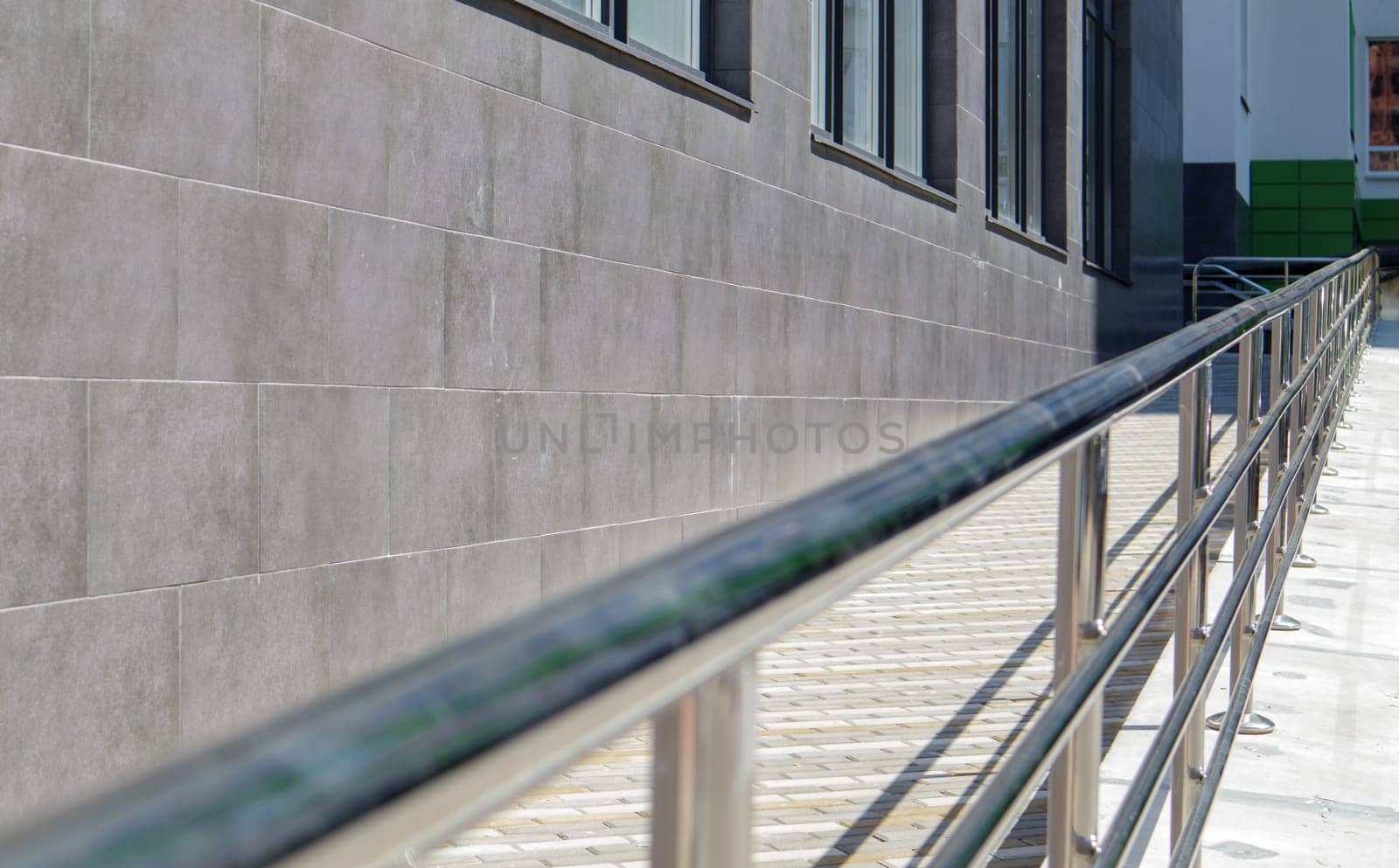 A ramp with stainless steel handrails for wheelchairs, bicycles and strollers with children in front of the building. Handrail for lifting a wheelchair. Shiny stainless steel handrail
