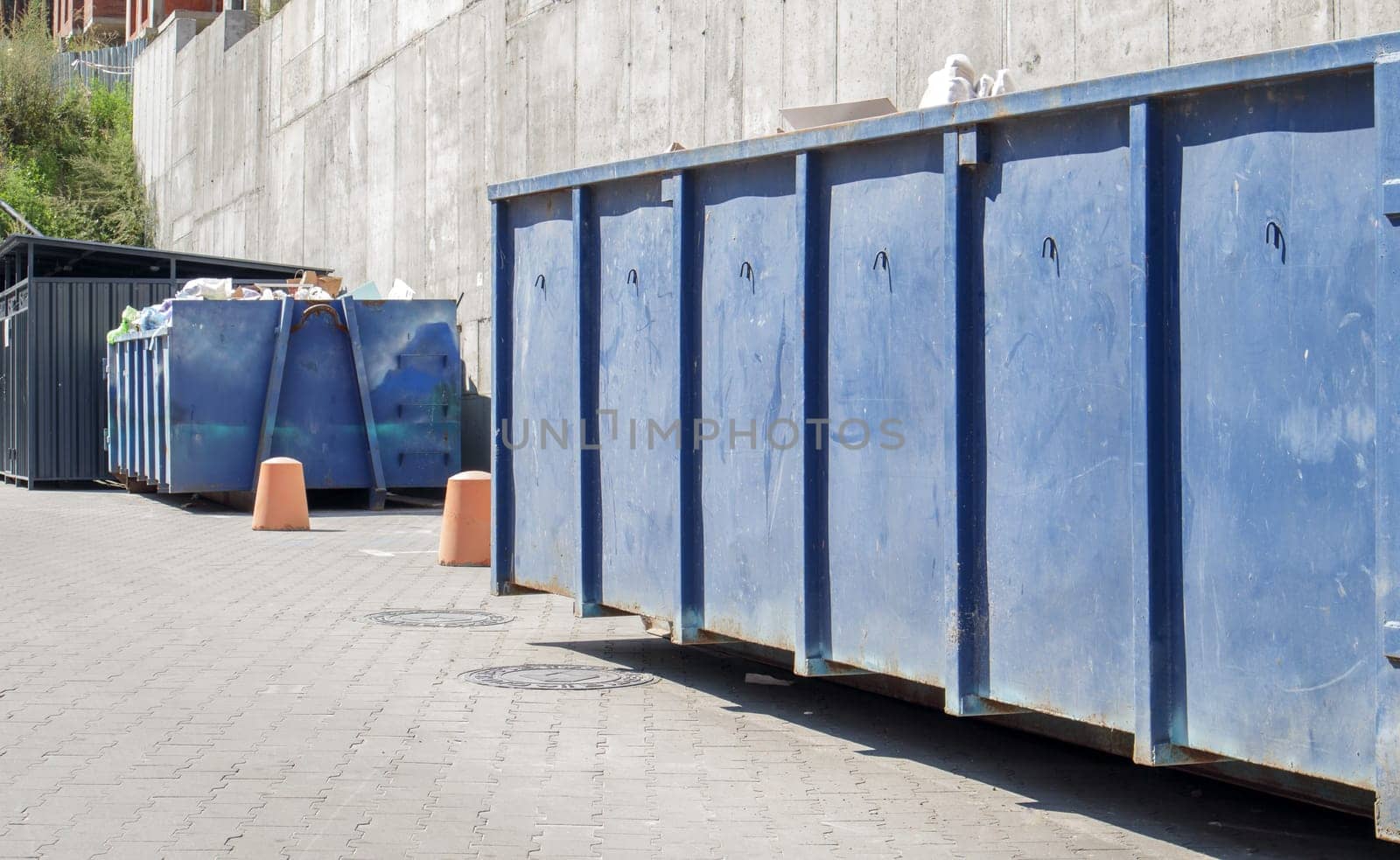 Metal durable blue industrial trash bin for outdoor trash at construction site. Large waste basket for household or industrial waste. A pile of waste