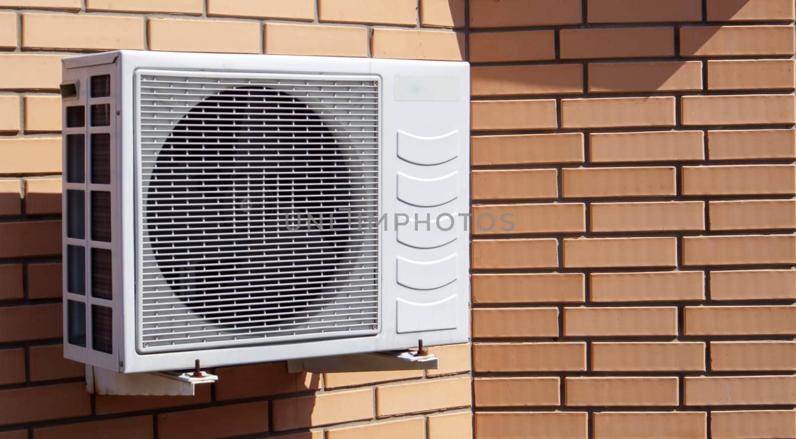 Close-up shot of a modern climate control unit against the background of a brick wall of the facade of a house outside. Air conditioner on the wall with space for text. Air compressor