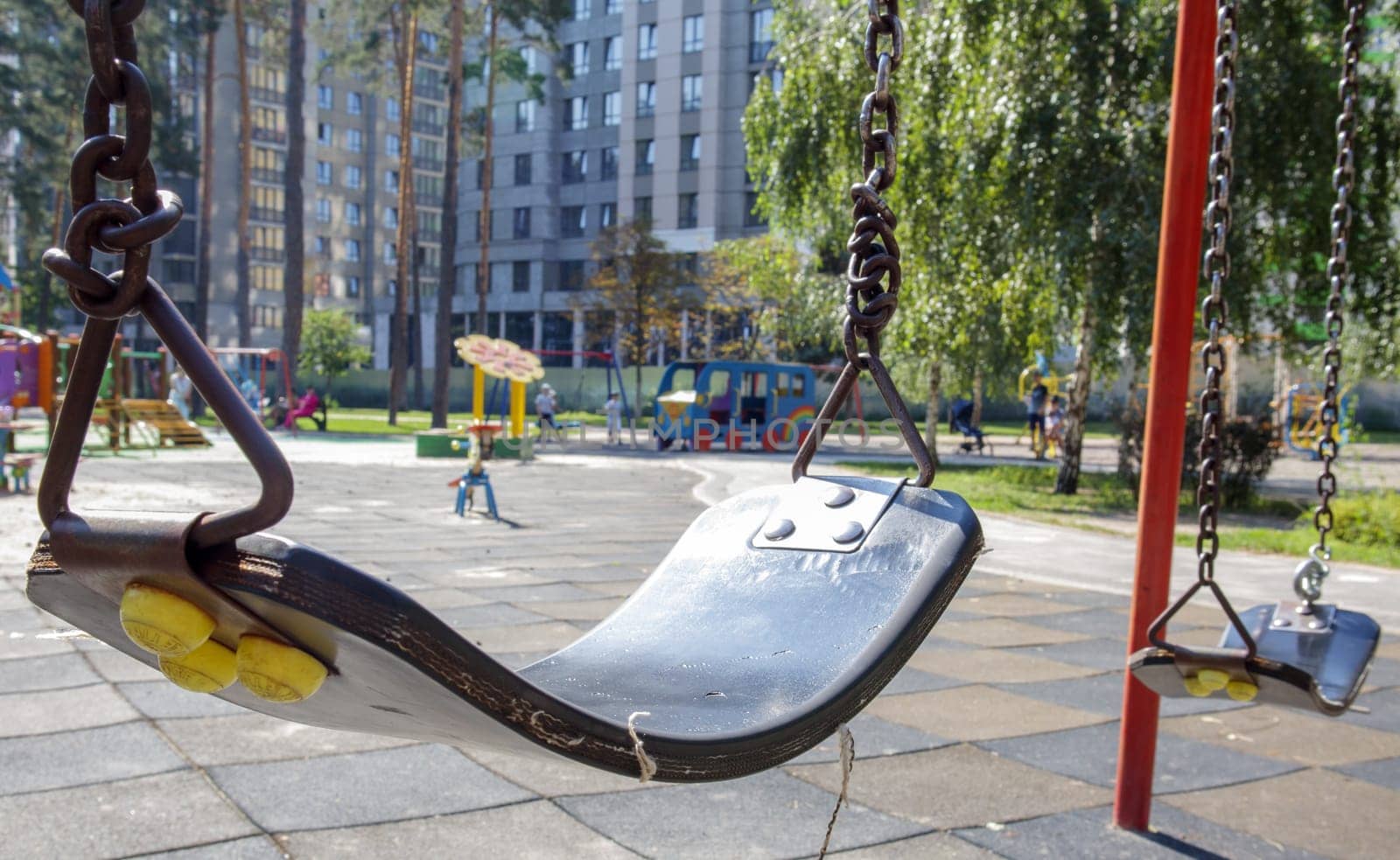 Close up empty baby swing in the park. New chain swing. Set of black swing chains on a modern playground. Focus on the swing in the blurry background. Ukraine, Kiev - August 19, 2021
