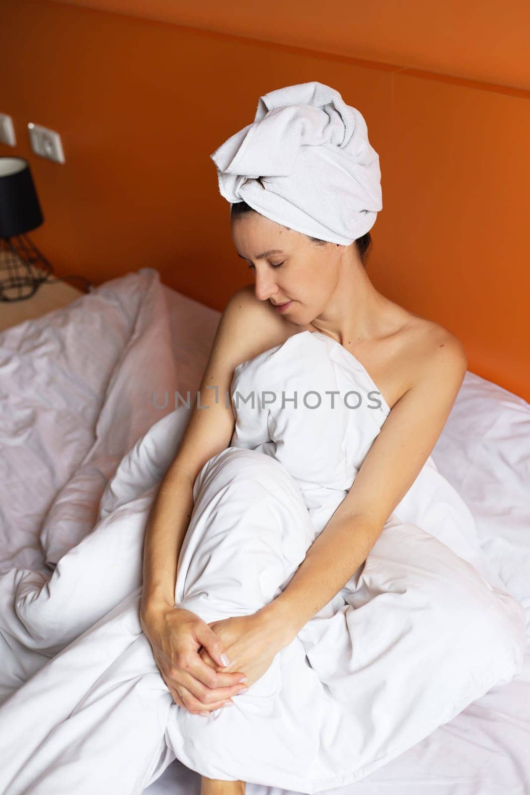 Young girl with clean skin with a towel on her head lying in bed, resting after a shower, relaxing at home