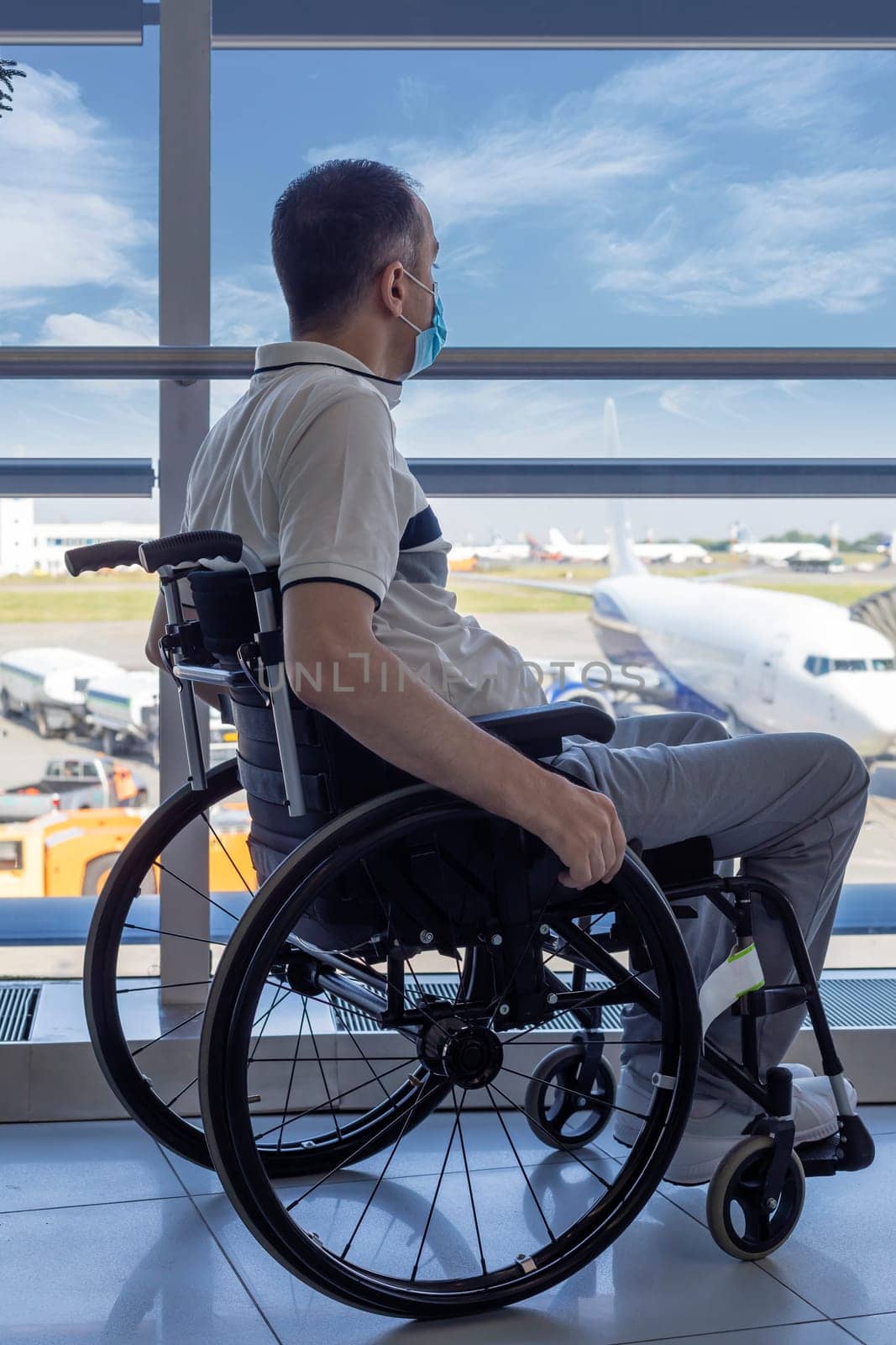 Young man with protective mask in a wheelchair at the airport looking out the window
