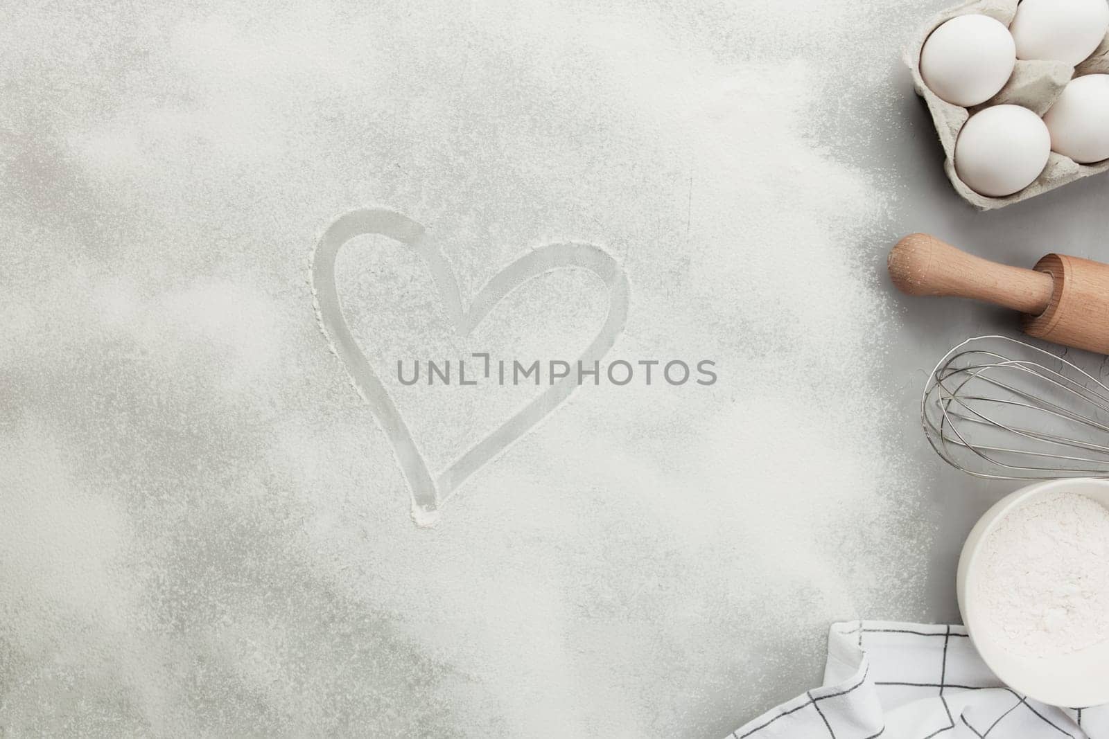 Heart shape from flour on grey concrete background flat lay, copy space. Baking ingredients, kitchen utensils, cooking hobby concept. Prepare dough, egg, bowl flour, rolling pin, whisk, kitchen towel