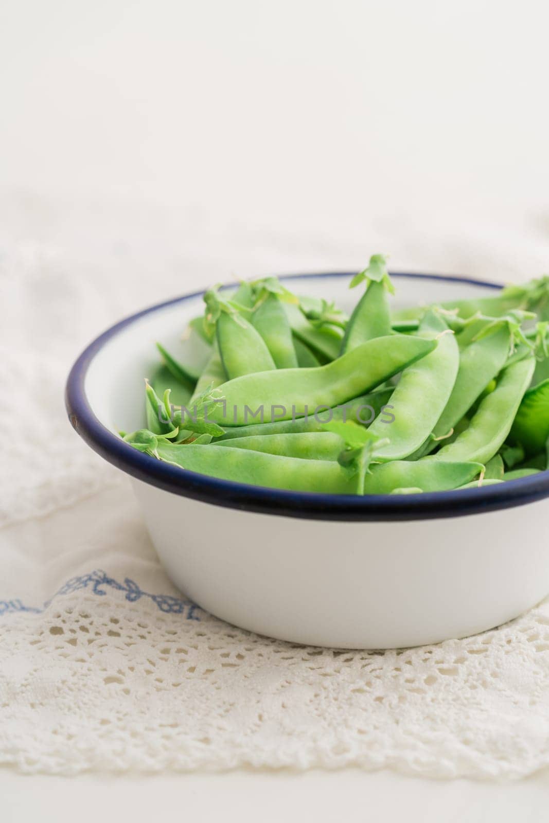 Sugar snaps in white enamel bowl on a table with vintage lace tablecloth
