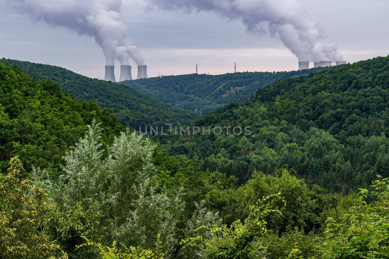Valleys covered with forest and on the horizon are the cooling towers of a nuclear power plant Dukovany. Contrast of nature and industry. Czech republic.