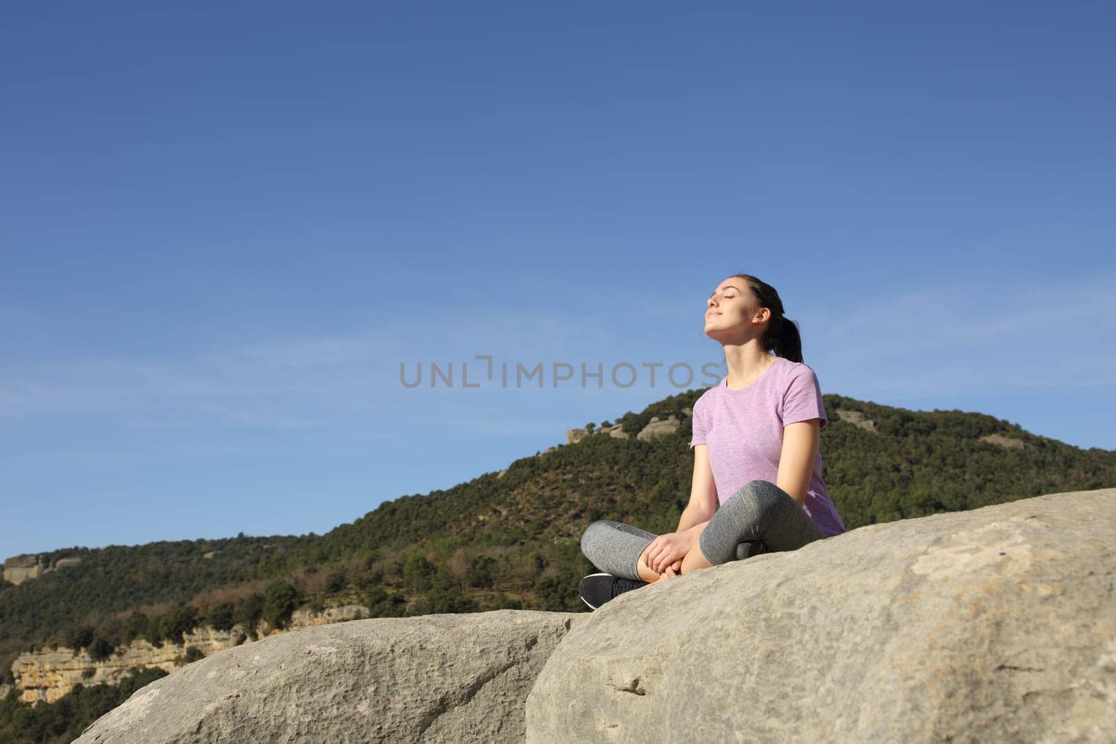Sportswoman relaxing resting seated in the top of a cliff in the mountain a sunny day