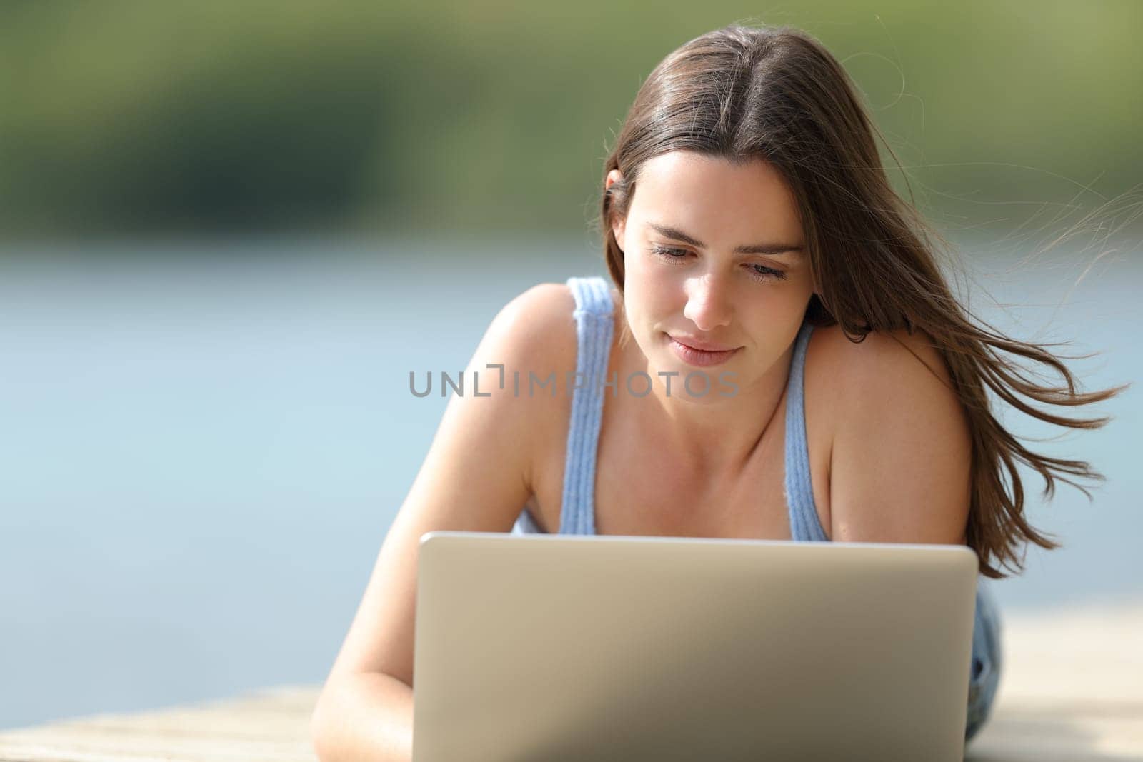 Front view portrait of a woman checking laptop content in a lake pier