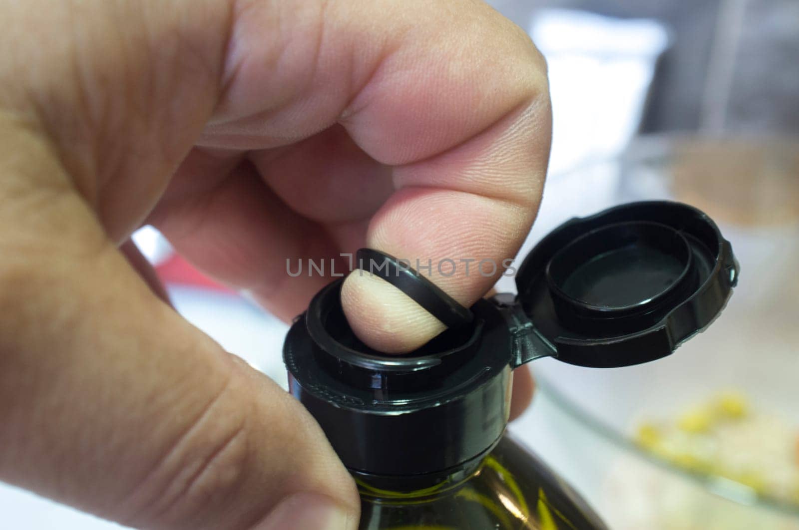 Finger opening a sealed olive oil bottle with an inner pull-off plastic tab underneath the cap. Closeup