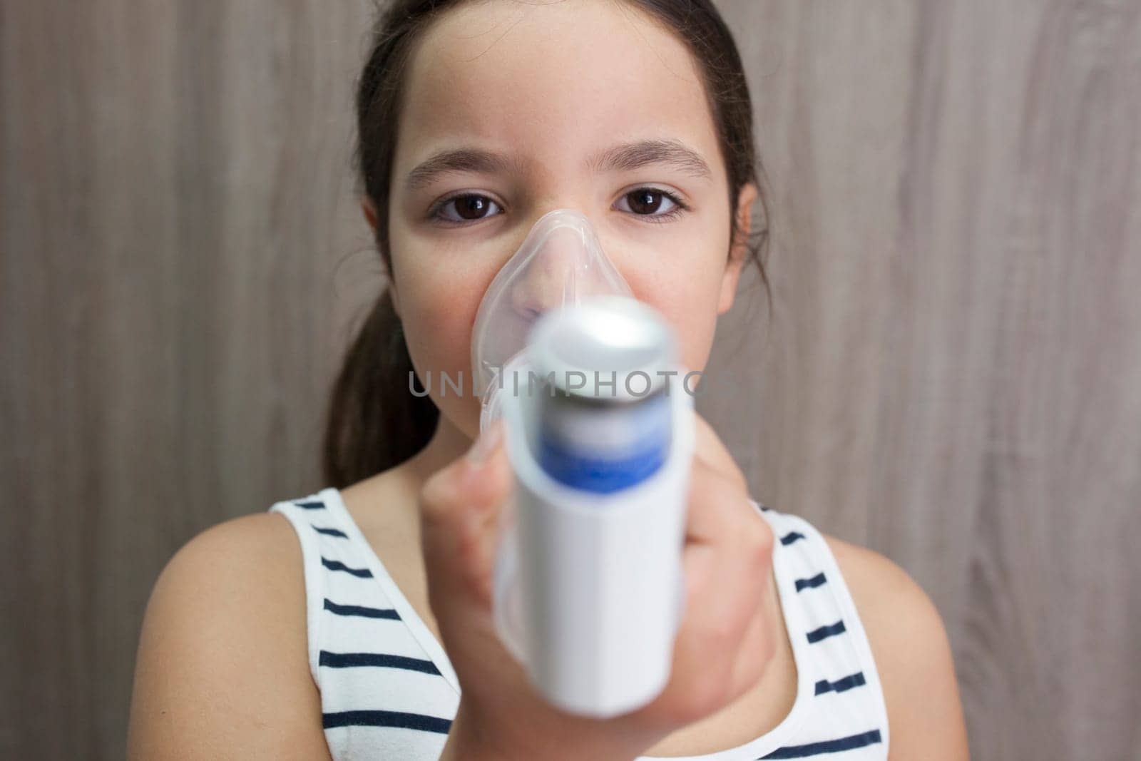 Child girl using medical spray for breath. Inhaler, spacer and mask. Front view