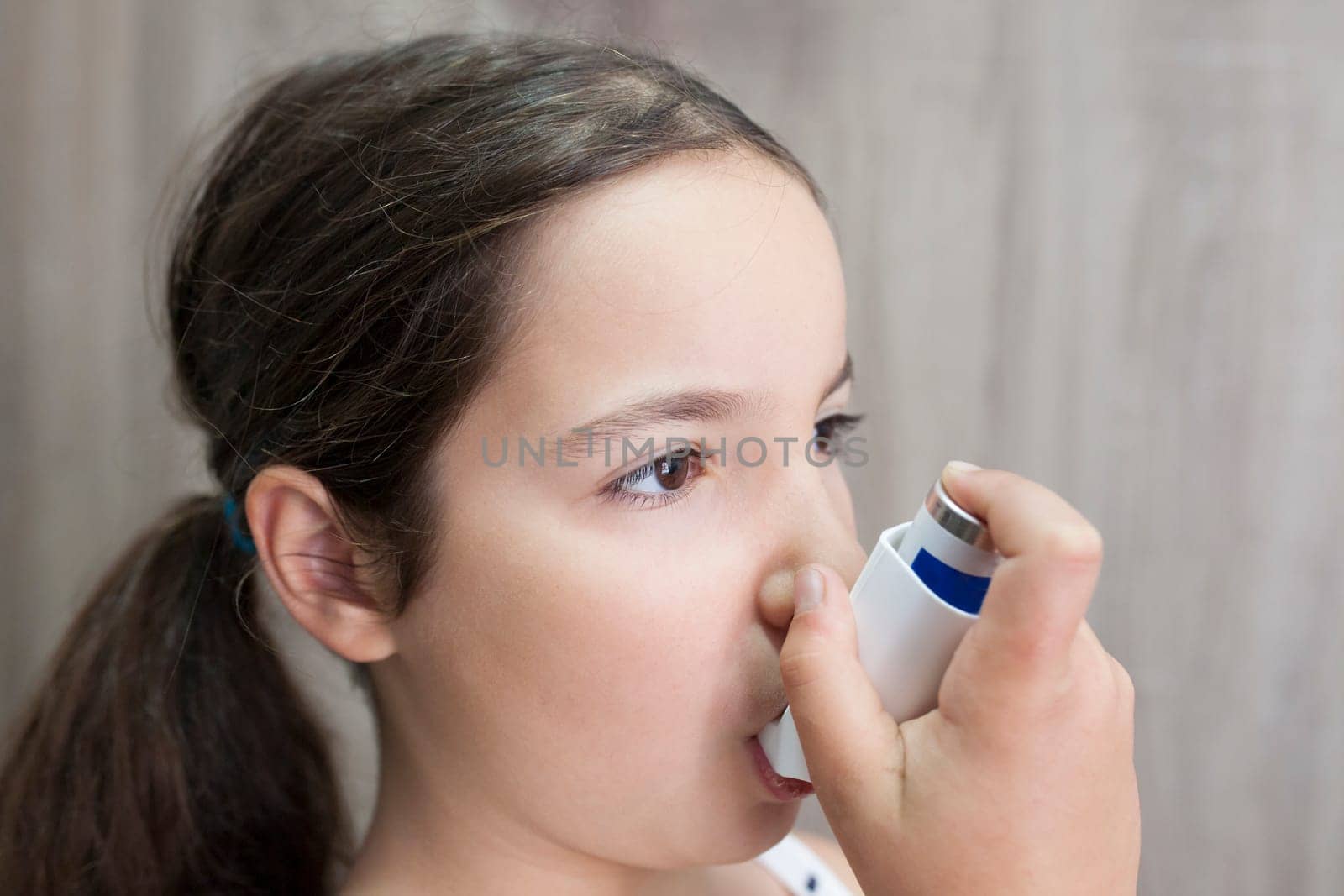 Child girl using medical spray for breath. Inhaler. Side view