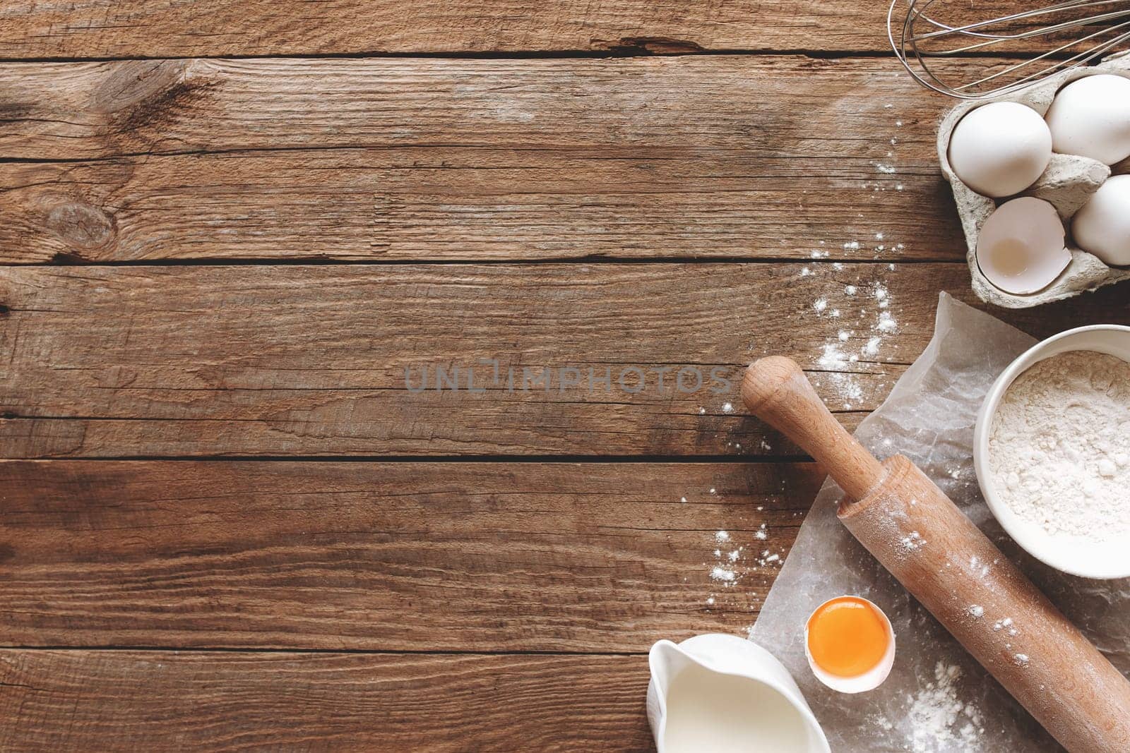 Baking ingredients, kitchen utensils on old wooden background. Cooking dough, preparing egg yolk, flour, rolling pin, milk, parchment paper, whisk, salt, sodium. Concept flat lay photo with copy space