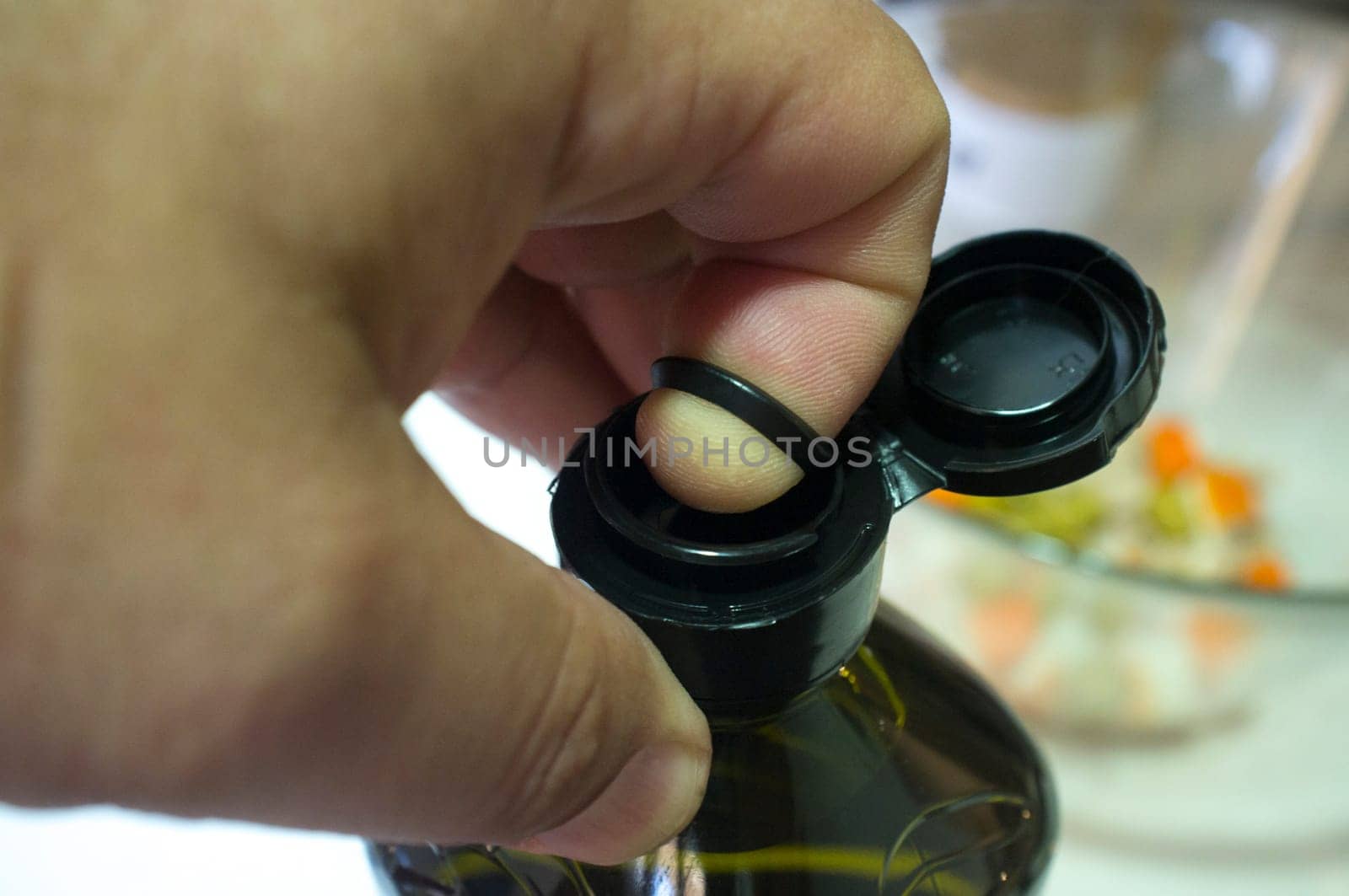 Finger opening a sealed olive oil bottle with an inner pull-off plastic tab underneath the cap. Closeup