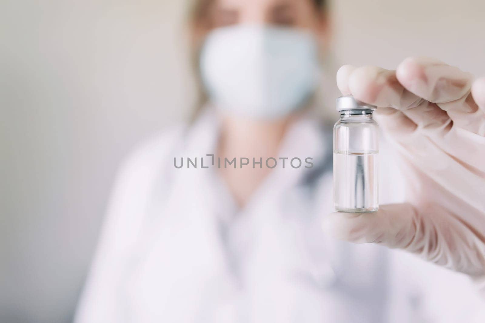 Woman doctor or nurse in uniform and white gloves wearing face mask protective in lab, holding medicine liquid vaccine vial bottle preparing for injection with COVID-19 Coronovirus vaccine for patient