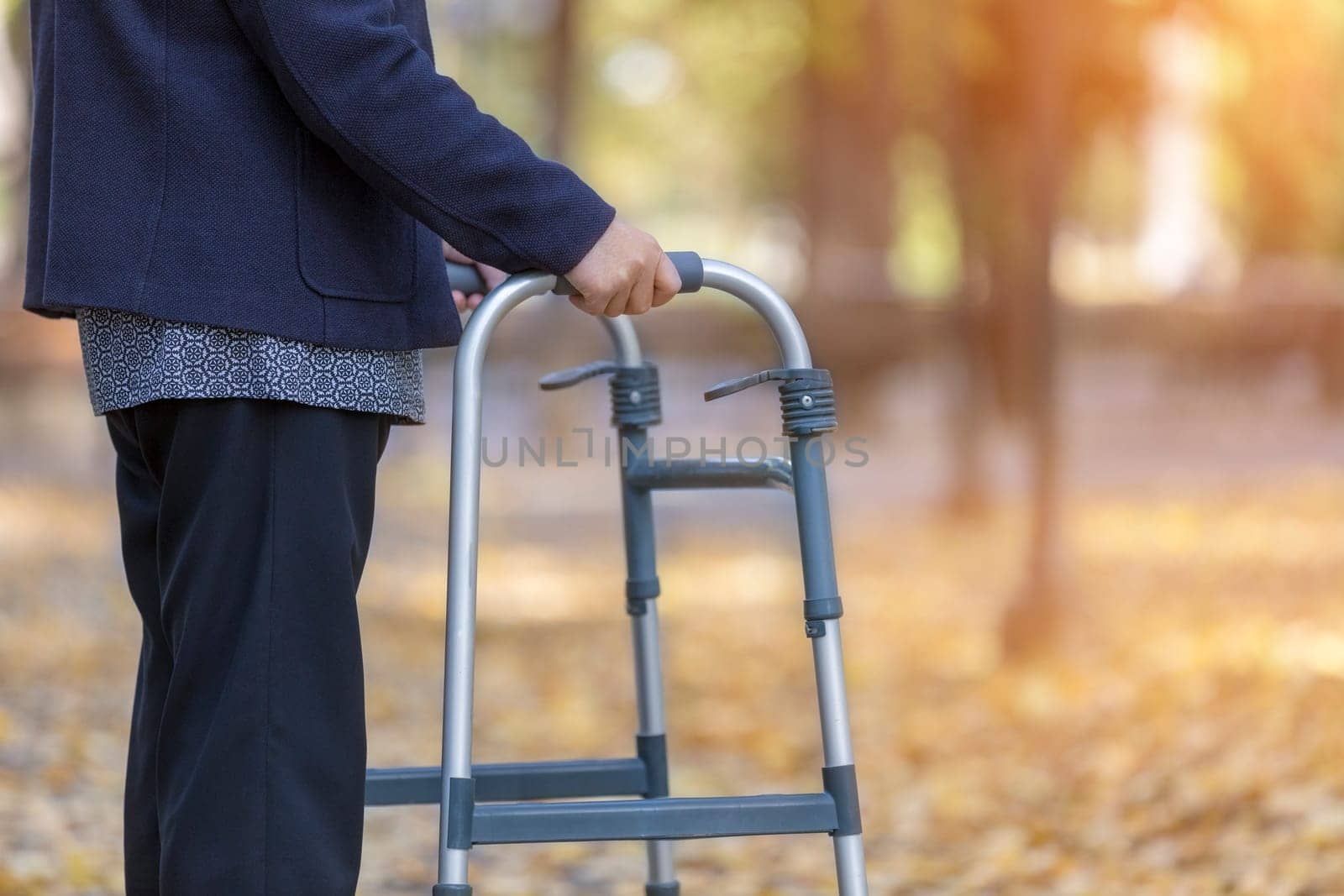 Woman with walker walking in autumn park closeup. Focus on her hand.