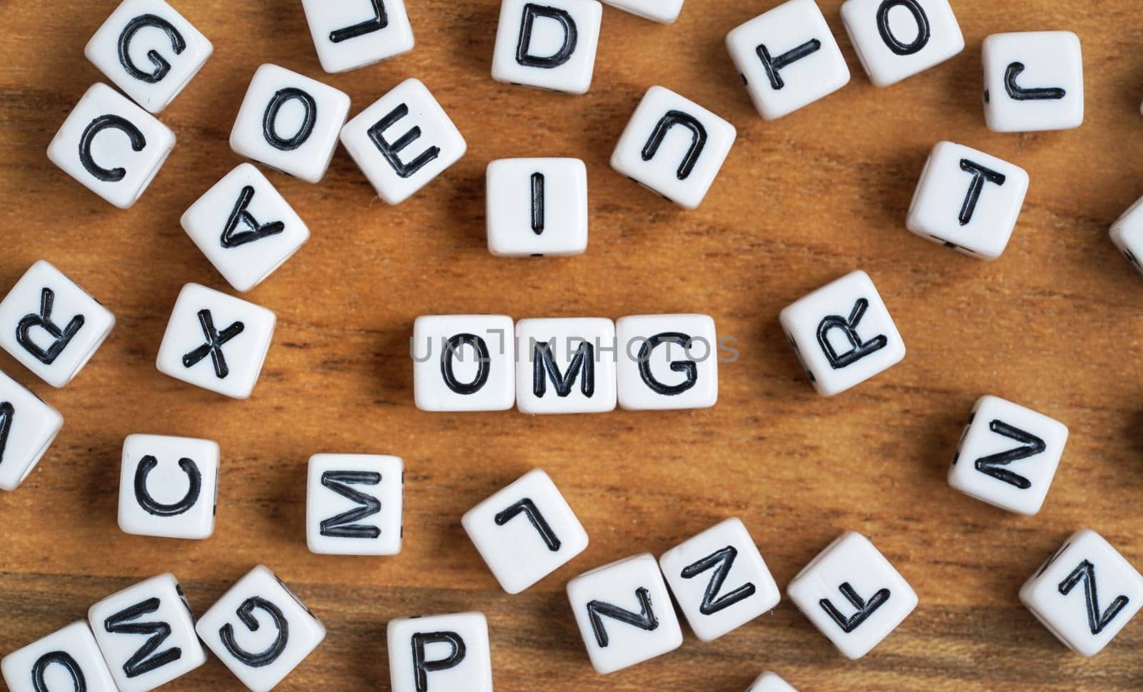 Small white and black bead cubes on wooden board, letters in middle spell OMG.