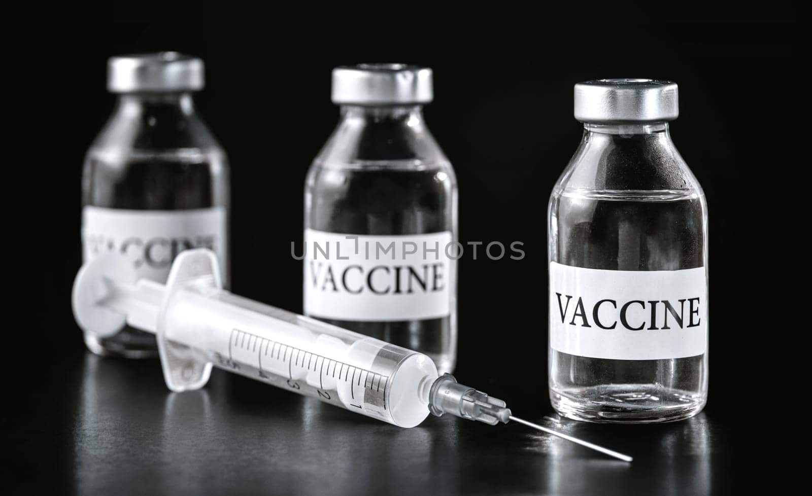 Three glass vaccine vials on black board, hypodermic syringe near.