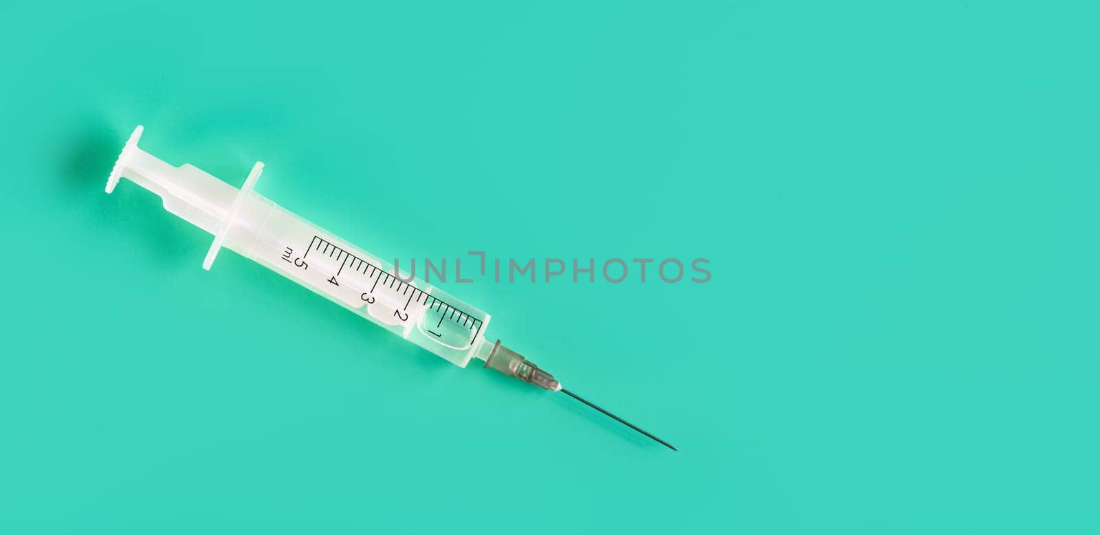 White injection syringe and needle with clear liquid on a green blue board, close-up detail from above, space for text right side.