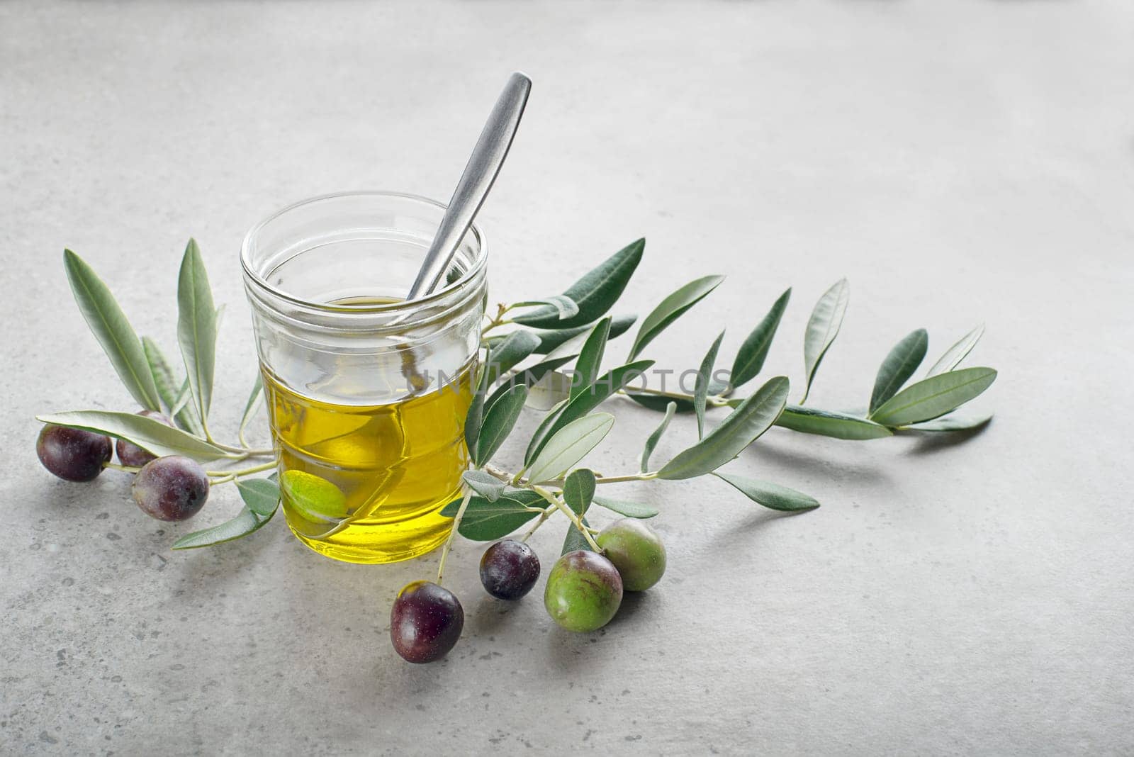 Glass of olive oil and Branch with olives and leaves background close up. Healthy olive oil concept