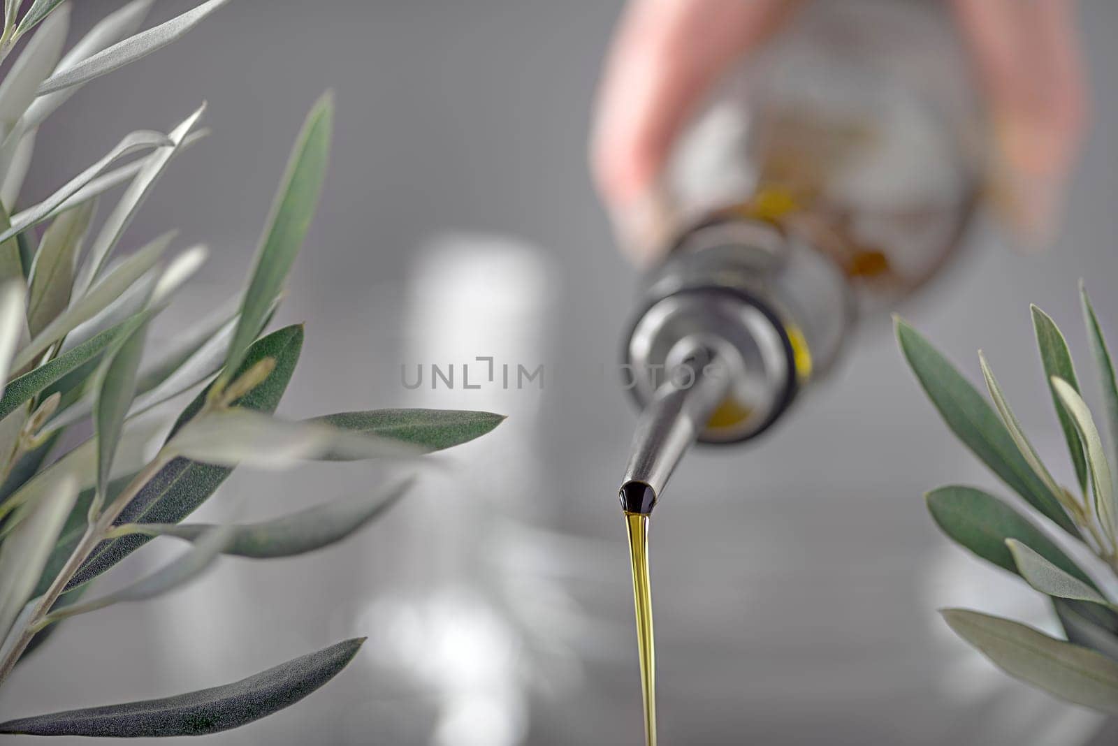 Bottle pouring virgin olive oil with olive branch background. Hand of cook pouring olive oil