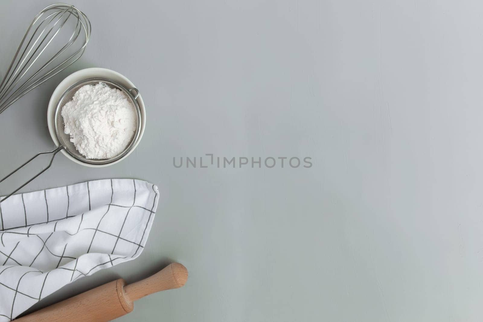 Baking ingredients, kitchen utensils, cooking concept on grey background flat lay, copy space. Prepare dough, bowl flour, rolling pin, whisk, kitchen towel, salt, soda, sieve. Photo on kitchen table