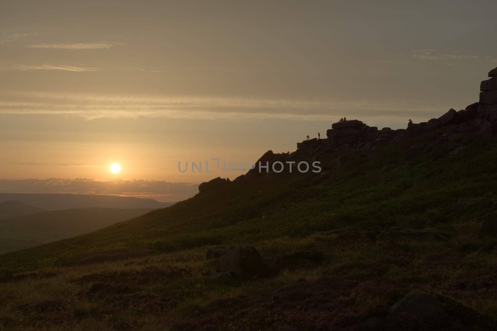 Climbers, couples and tourists line the rocky ridge of stanage edge at sunset. Many people enjoying the outdoors, wide angle perspective.