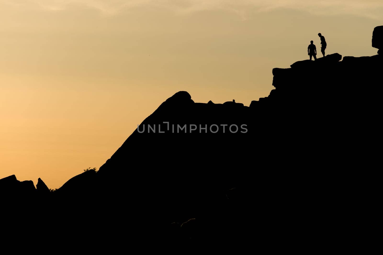 A pair of rock climbers, silhouetted at sunset, look back from the summit of stange edge. Located in the peak district in england. Outdoor activity