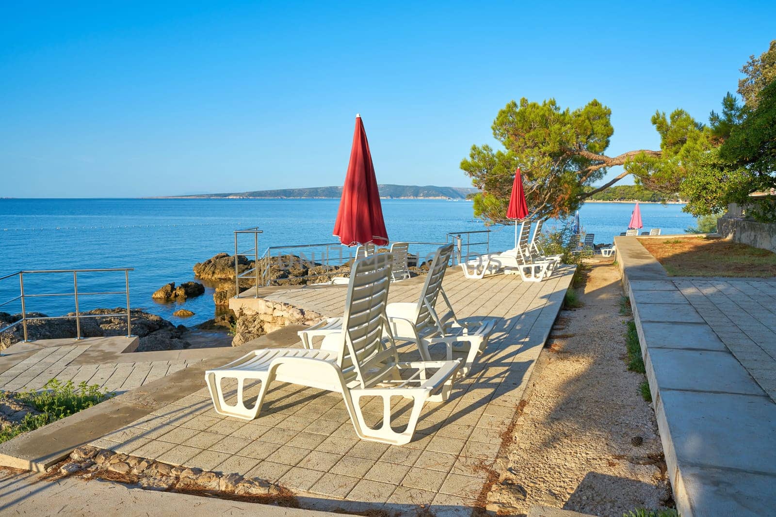 Parasols and sun loungers at a typical bathing place on the coast of the town of Krk on the Adriatic Sea in Croatia