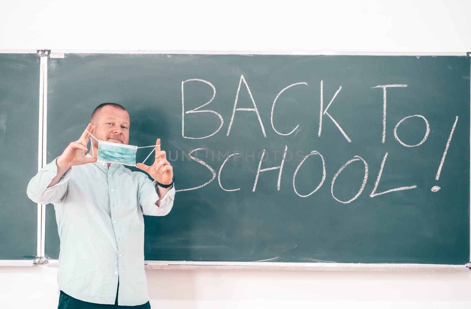 Teacher with face mask welcoming children back at school after lockdown. Back to school during COVID-19 pandemic.