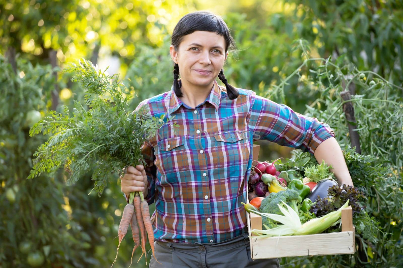 Farmer woman holding wooden box full of fresh raw vegetables. Growing organic food concept