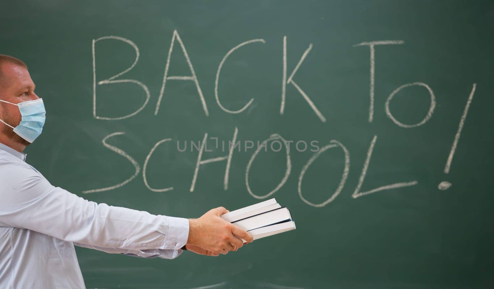 Teacher with face mask welcoming children back at school after lockdown. Back to school during COVID-19 pandemic.