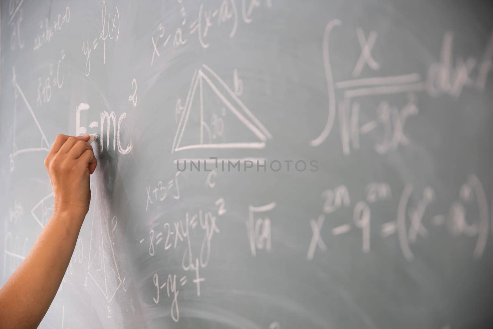 Close-up shot of a hand holding chalk and writing mathematical equations on the blackboard. Education concept.