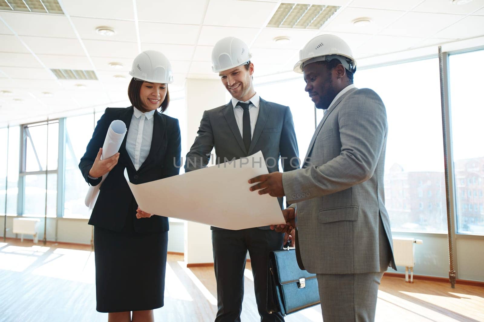 Confident architects in protective helmets discussing blueprint in office