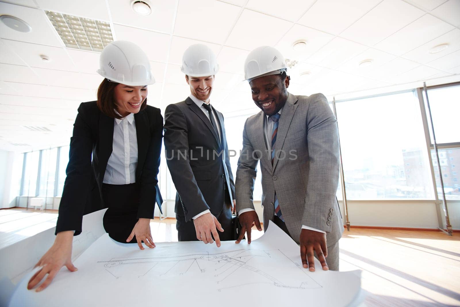 Confident architects in protective helmets looking at blueprint