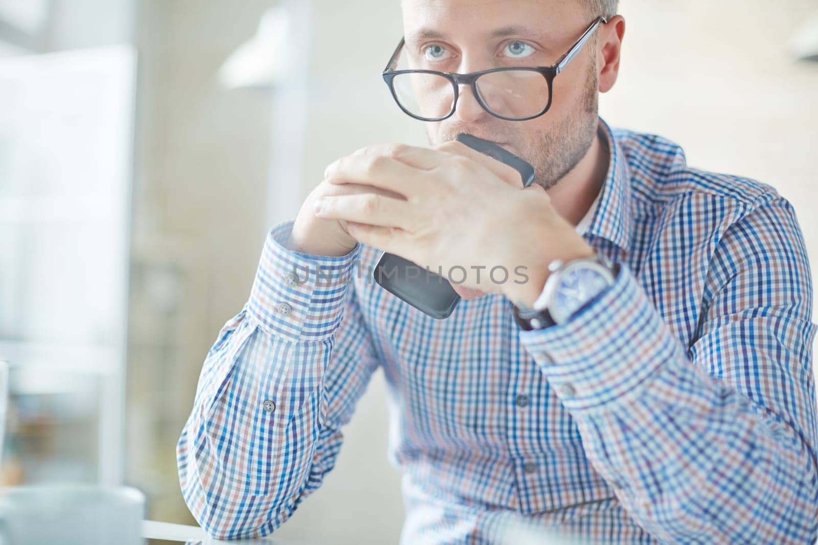 Serious businessman in eyeglasses holding cellphone