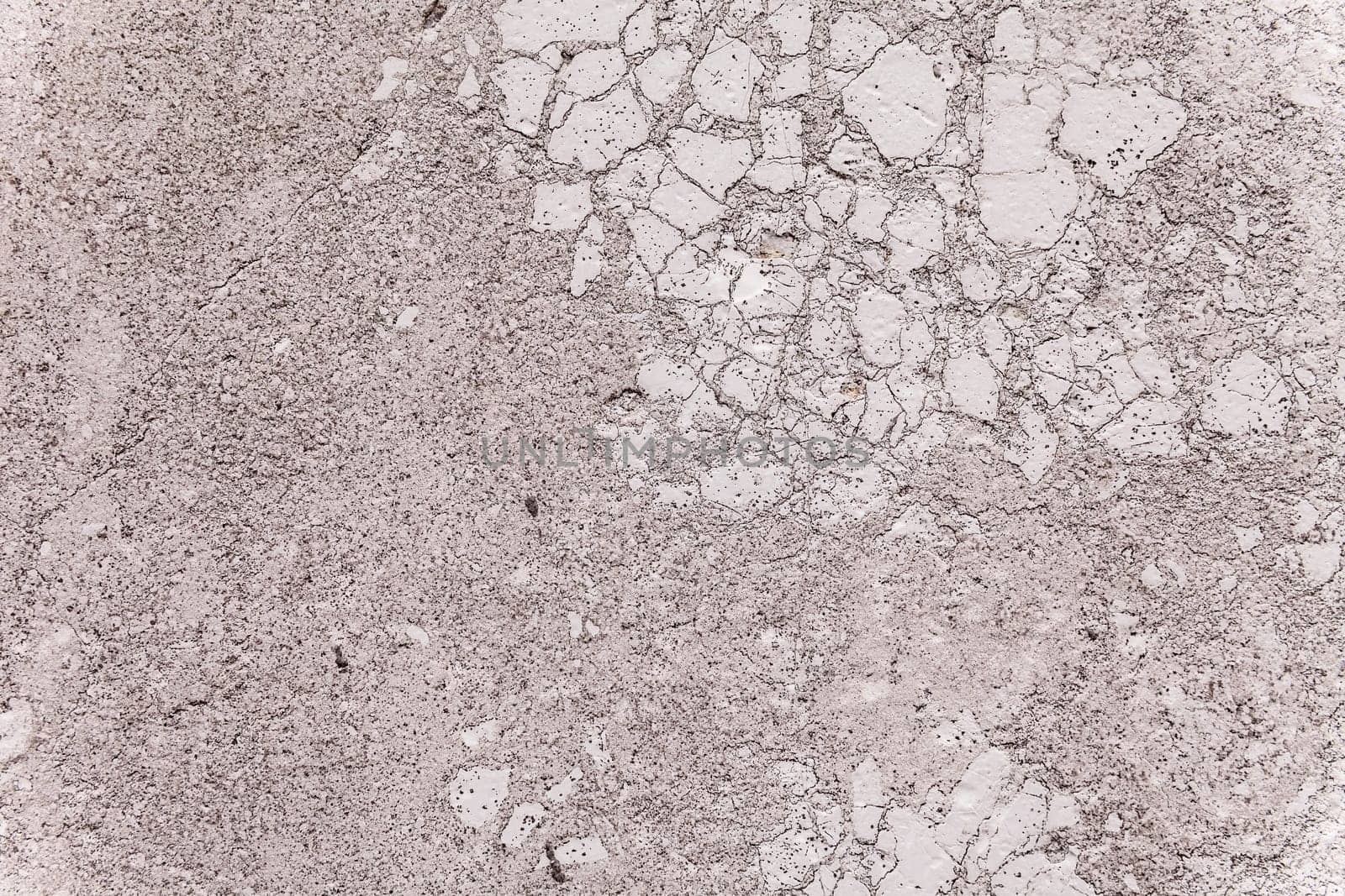 Close up on the brittle texture of plaster covering an exterior load-bearing wall. Porous surface, weather-worn patina. Two-dimensional architectural detail for background use. Gray color with spots.